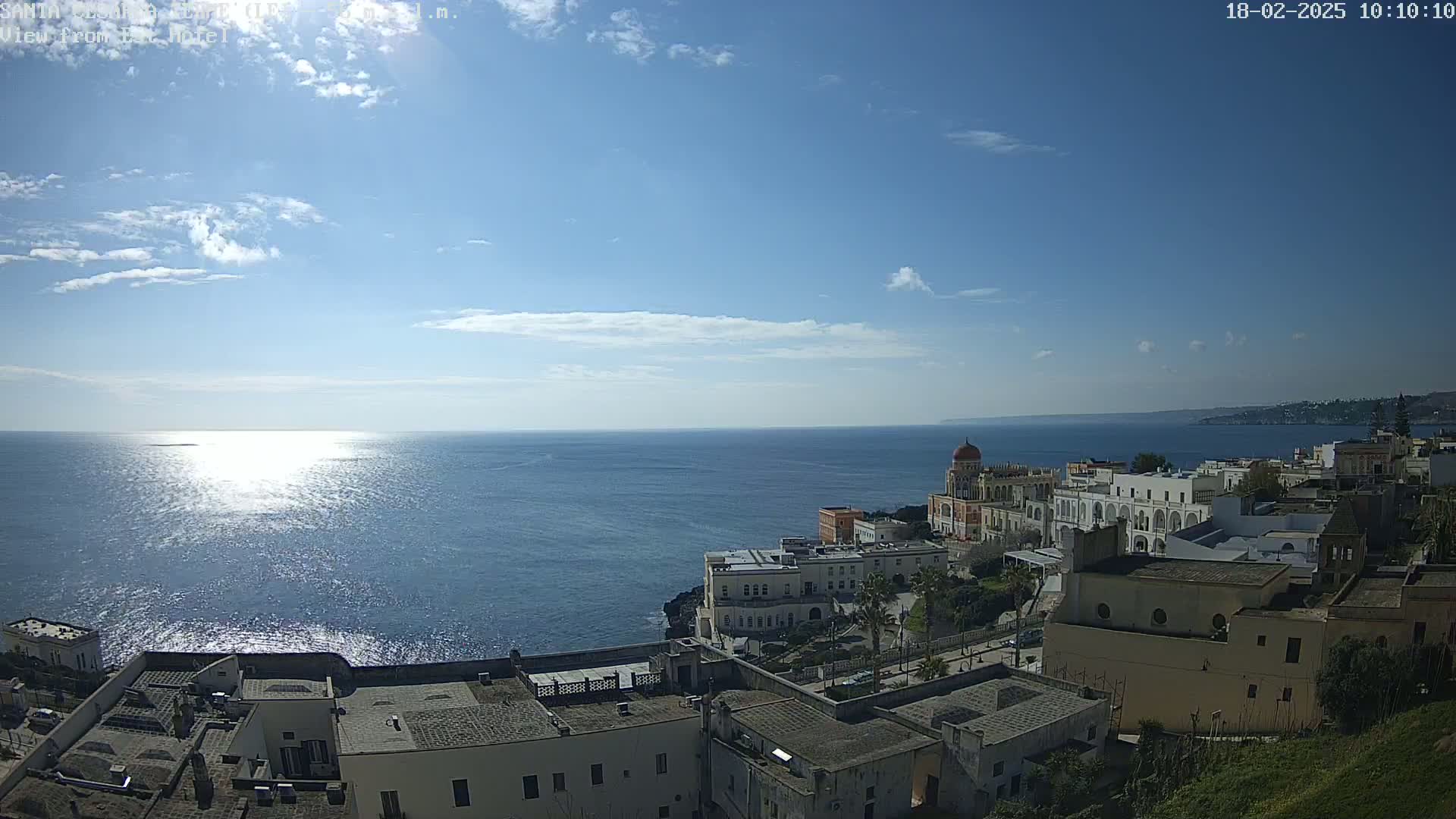 A coastal town overlooks a calm, sunlit sea under a mostly clear sky.