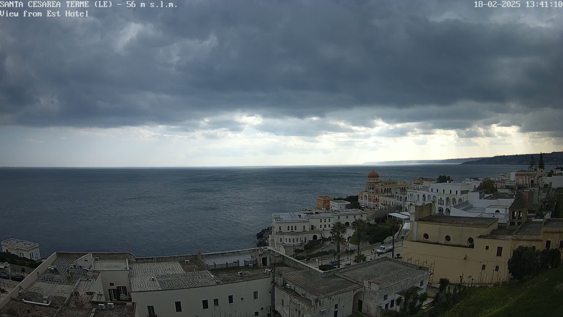 A coastal town with white buildings and a calm sea under a mostly cloudy sky.
