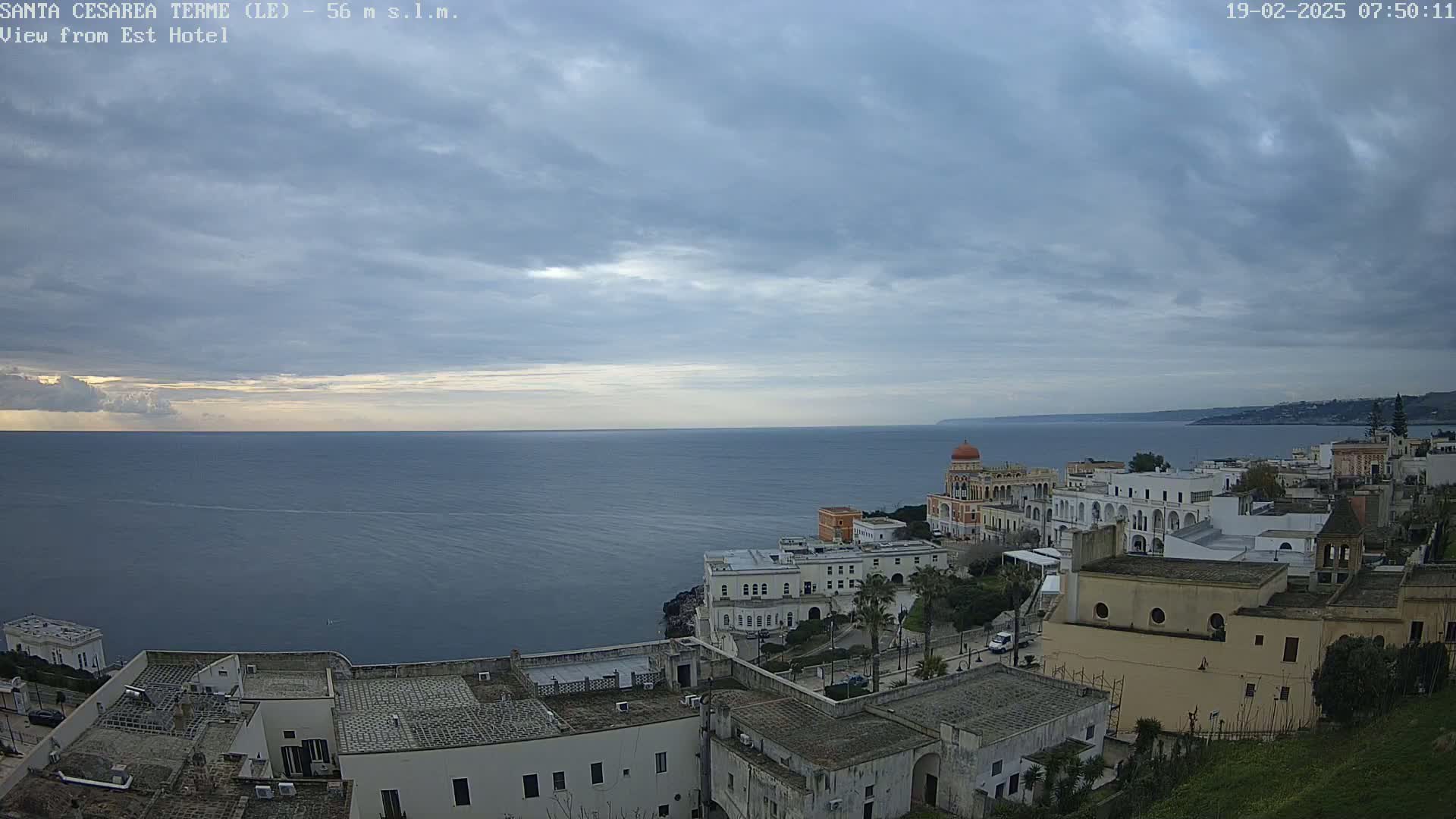 A coastal town with white buildings is shown under a cloudy sky, overlooking a calm sea.