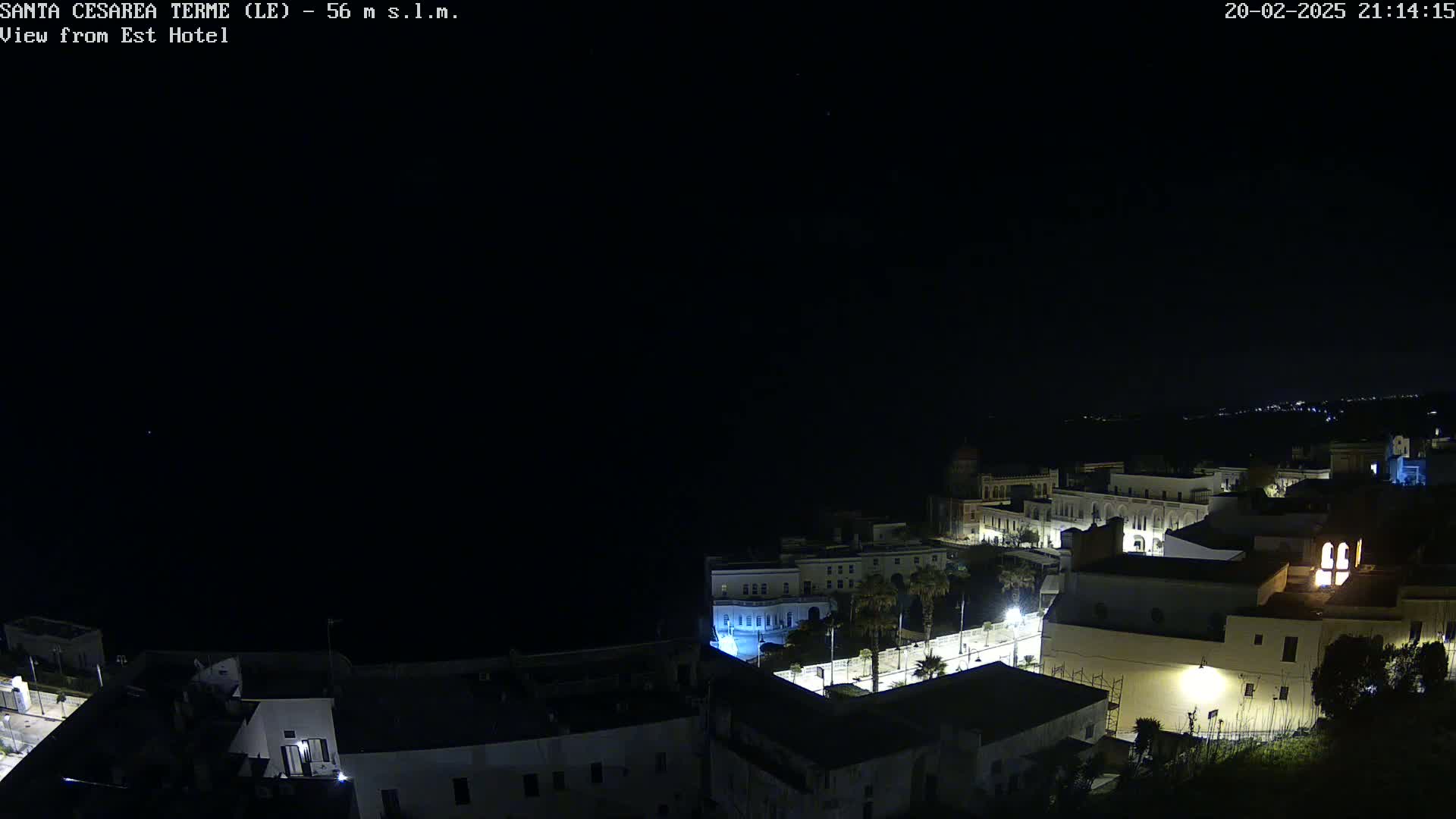 A nighttime, aerial view of a coastal town with buildings illuminated under a clear, dark sky.