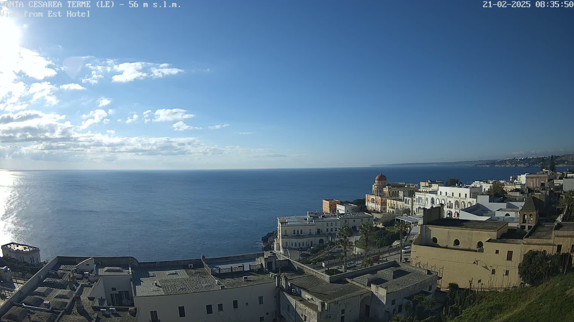 A partly sunny day reveals a coastal town overlooking a calm sea under a mostly clear blue sky.