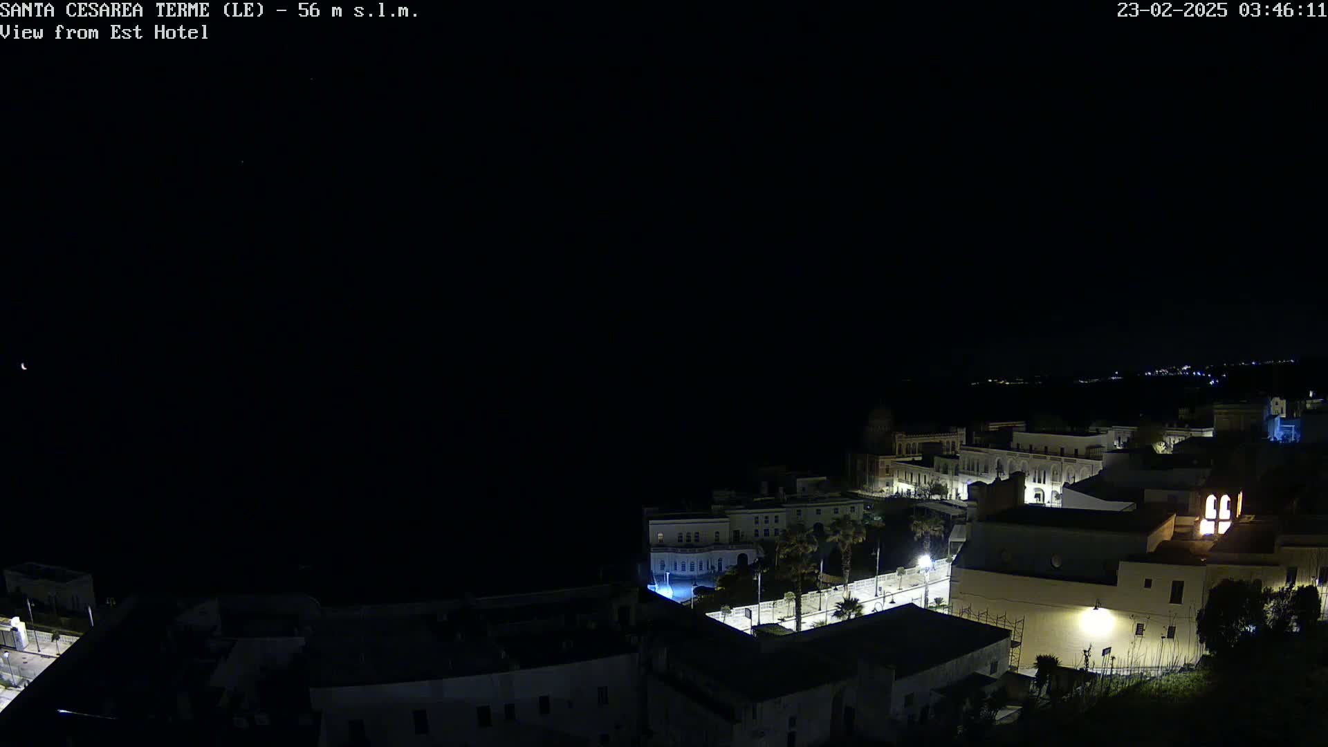 A nighttime, clear-sky view of a coastal town with buildings illuminated, seen from a high vantage point.