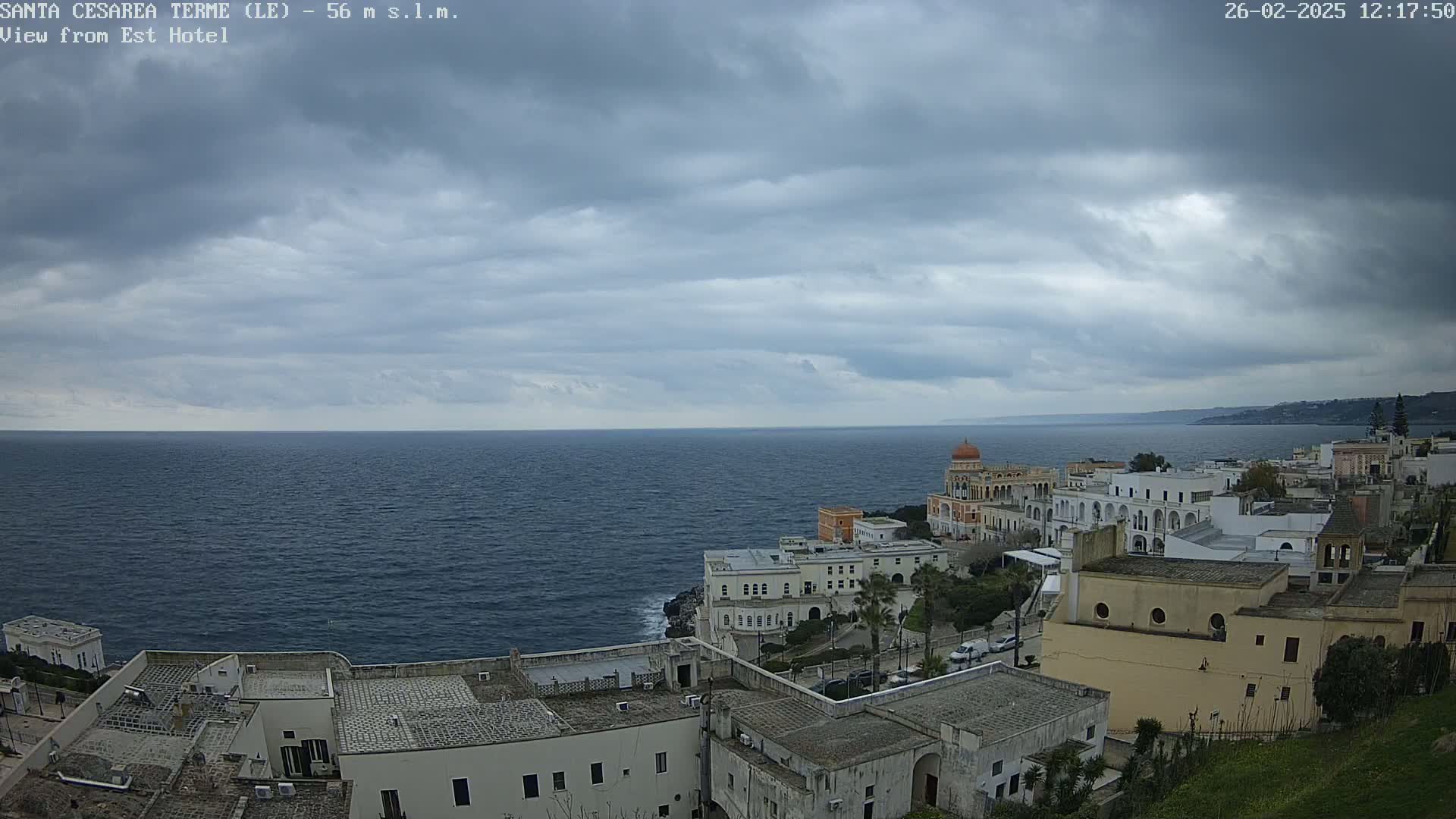 A coastal town with white buildings and a calm, dark-grey overcast sky sits overlooking a dark blue sea.