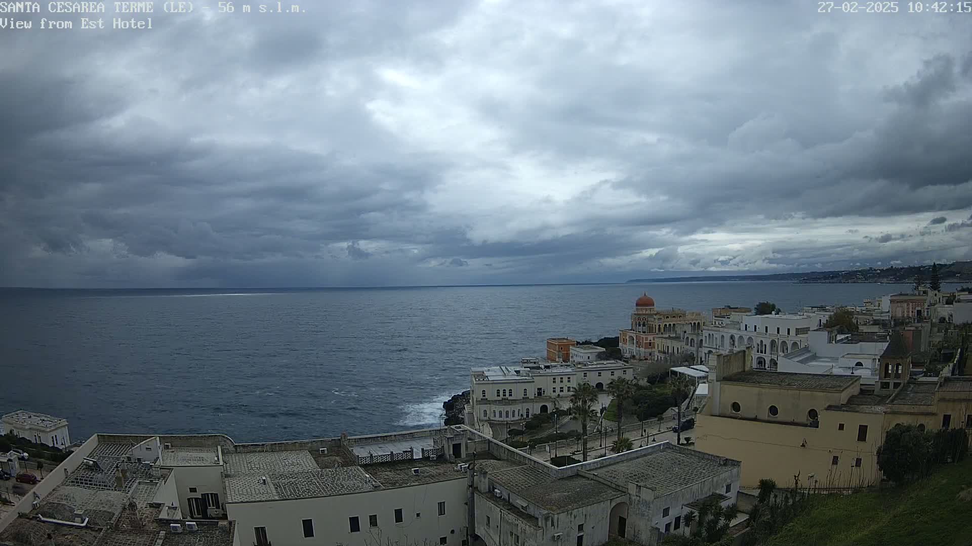 A coastal town with white buildings overlooks a dark, choppy sea under a cloudy sky.