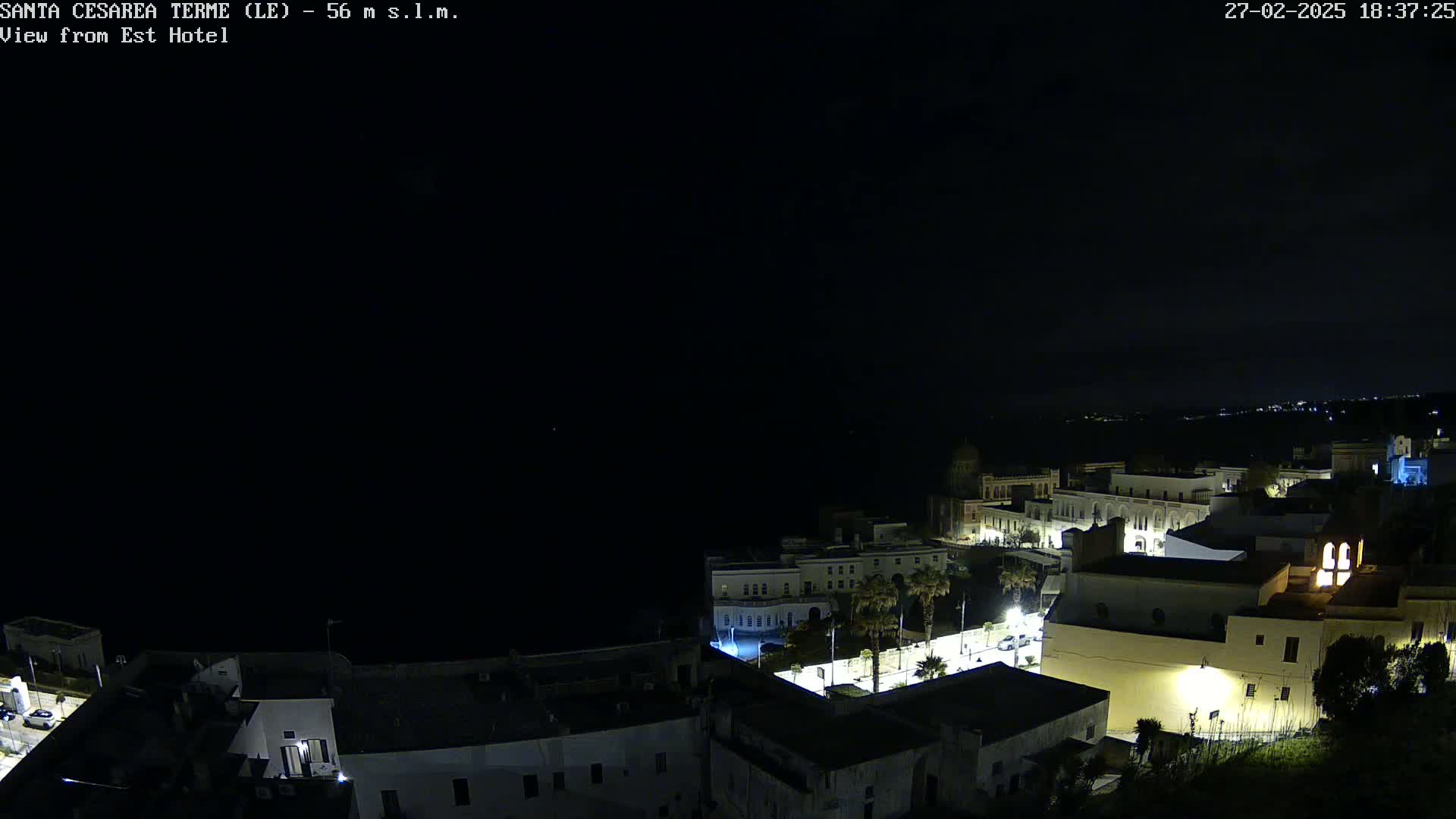 A nighttime view of a coastal town with buildings illuminated against a dark, clear sky.