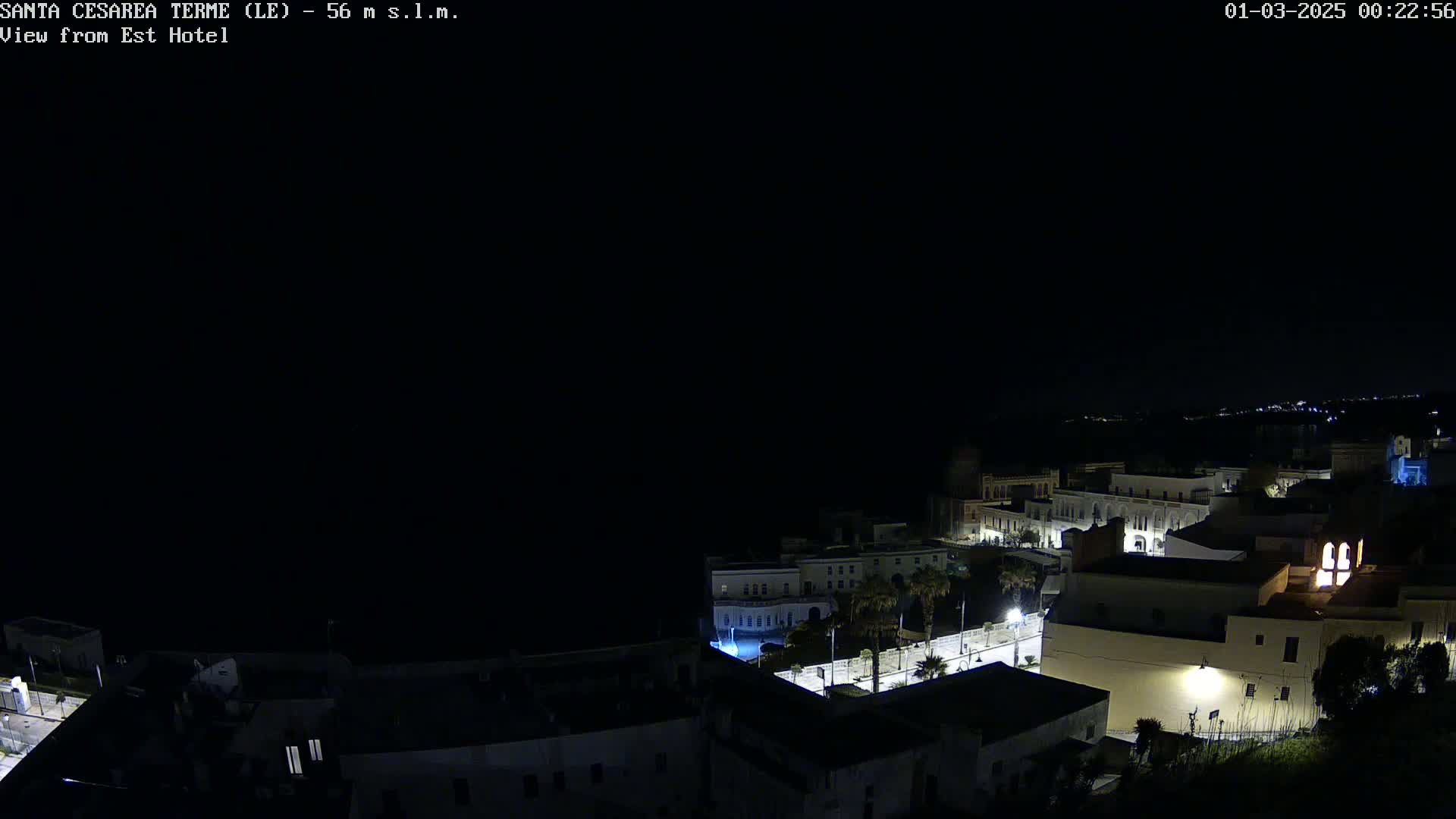 A nighttime, dark view of a coastal town with illuminated buildings and streets.