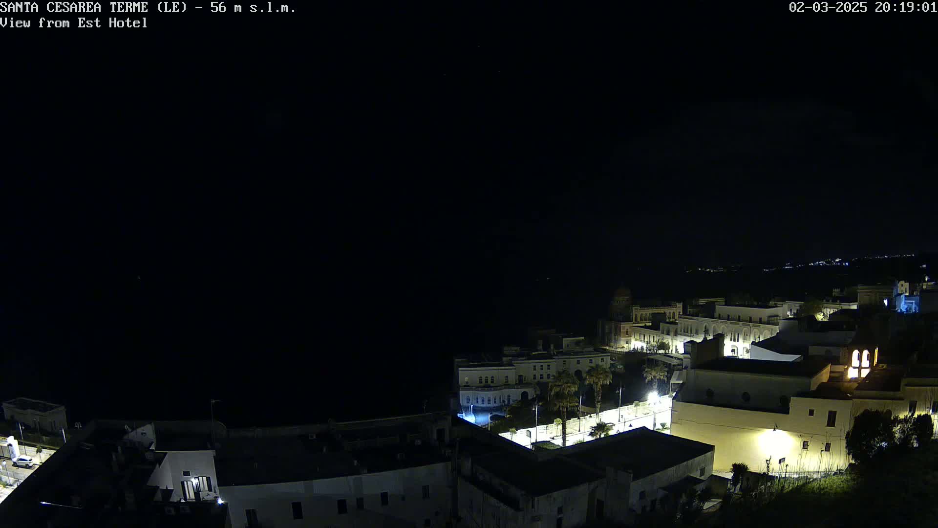 A nighttime, aerial view of a coastal town with buildings illuminated against a dark sky.