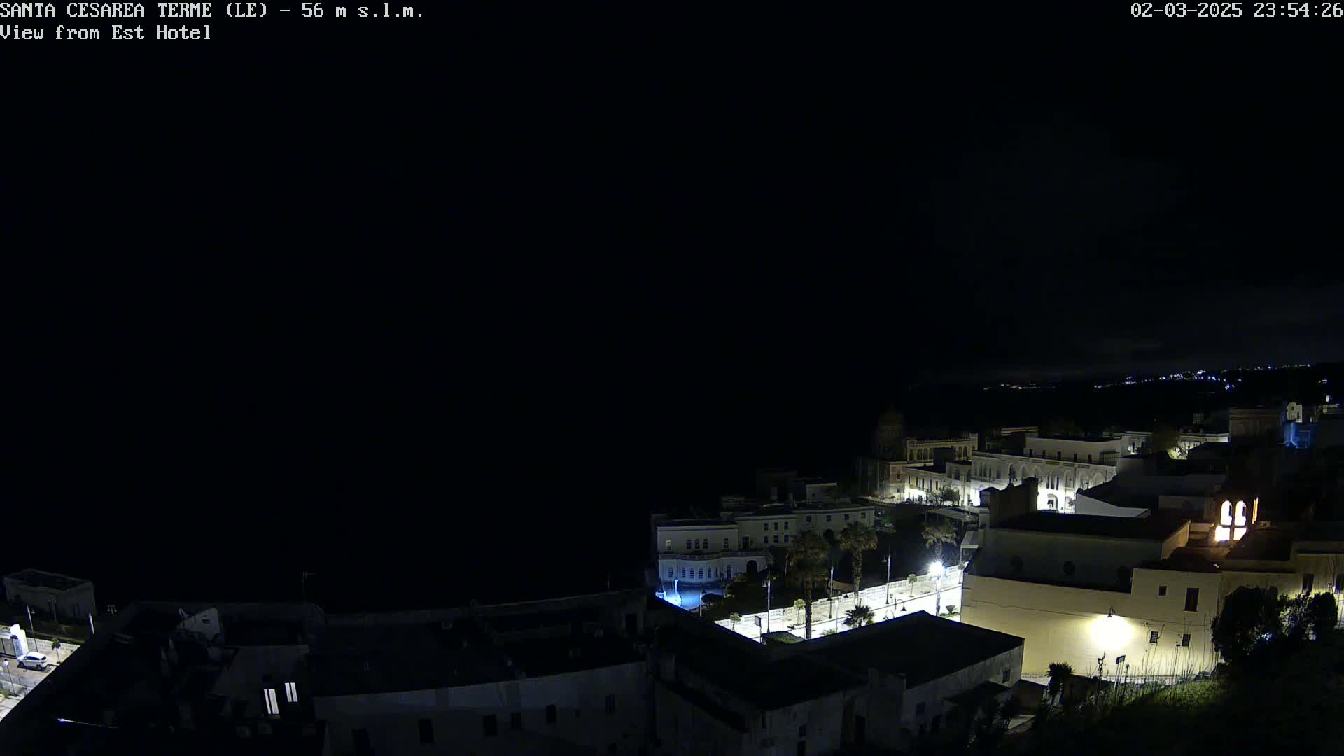 A nighttime, dark, aerial view of a coastal town with dimly lit buildings and streets.