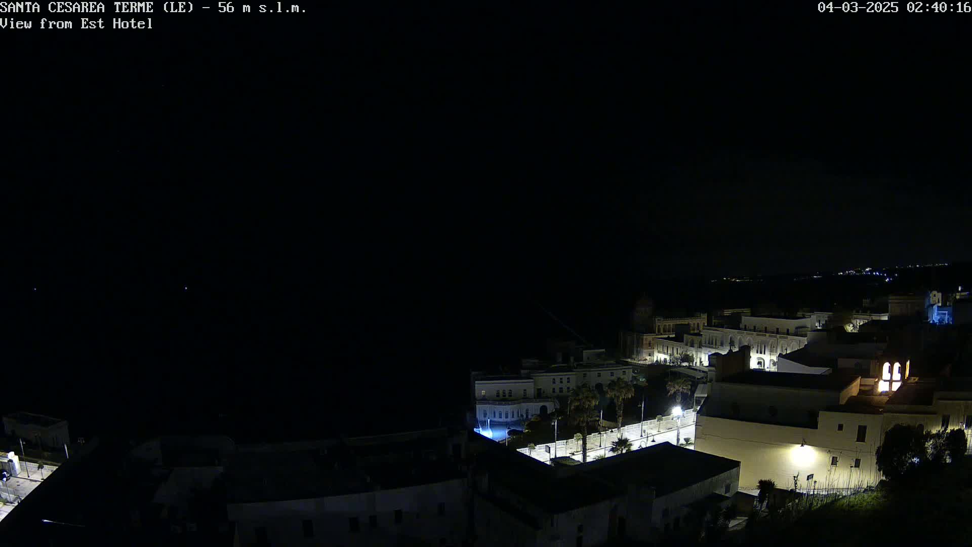 A nighttime, aerial view of a coastal town with dimly lit buildings under a dark, clear sky.