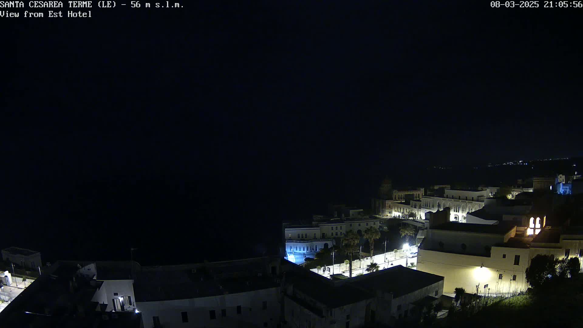 A nighttime, aerial view of a coastal town with dimly lit buildings and a dark sea.