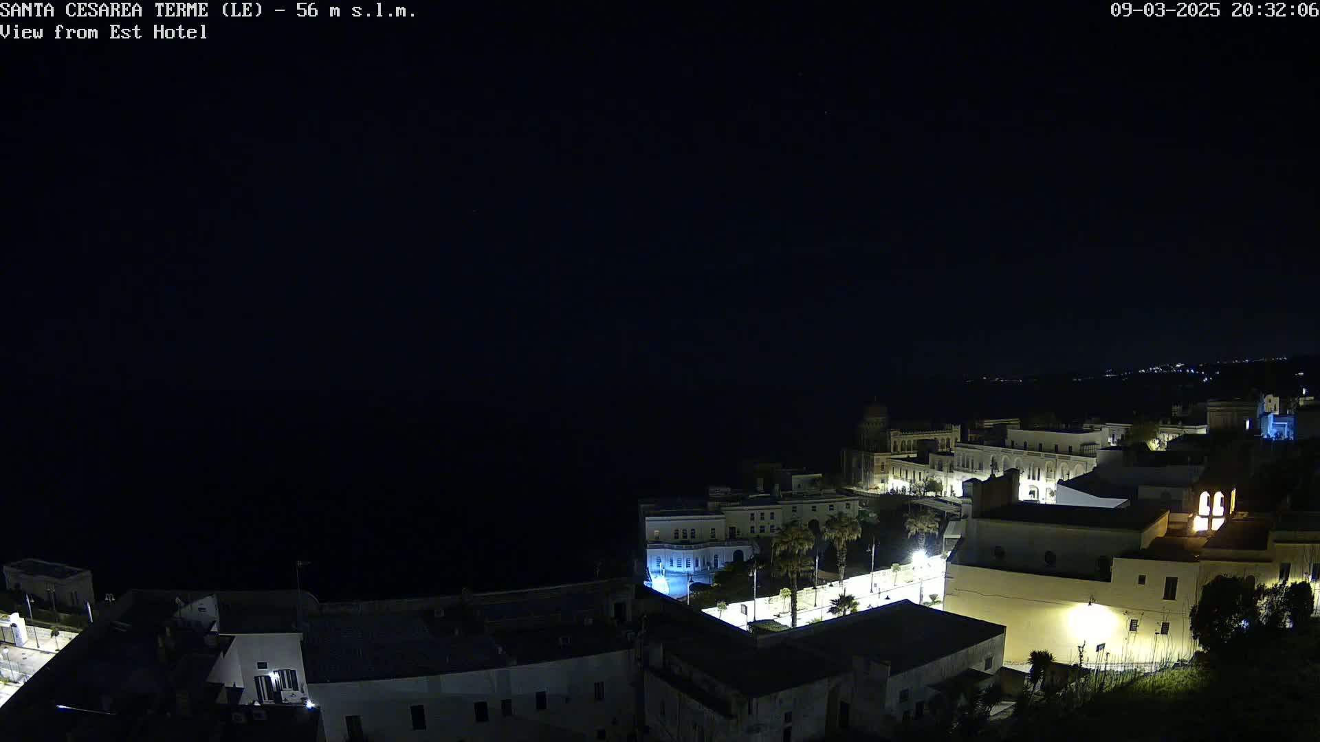 A nighttime coastal town with buildings illuminated, under a clear dark sky.