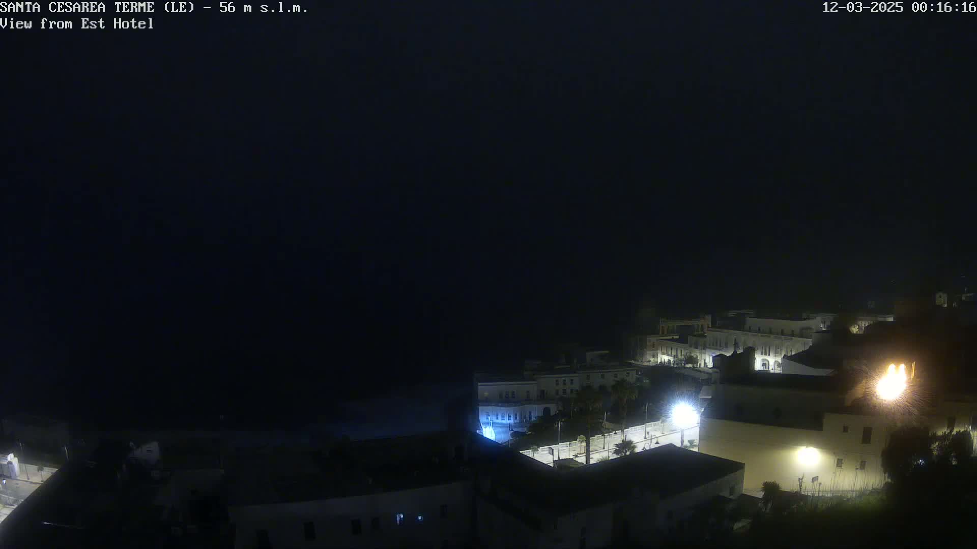 A nighttime, dark, and foggy view of a coastal town with dimly lit buildings.