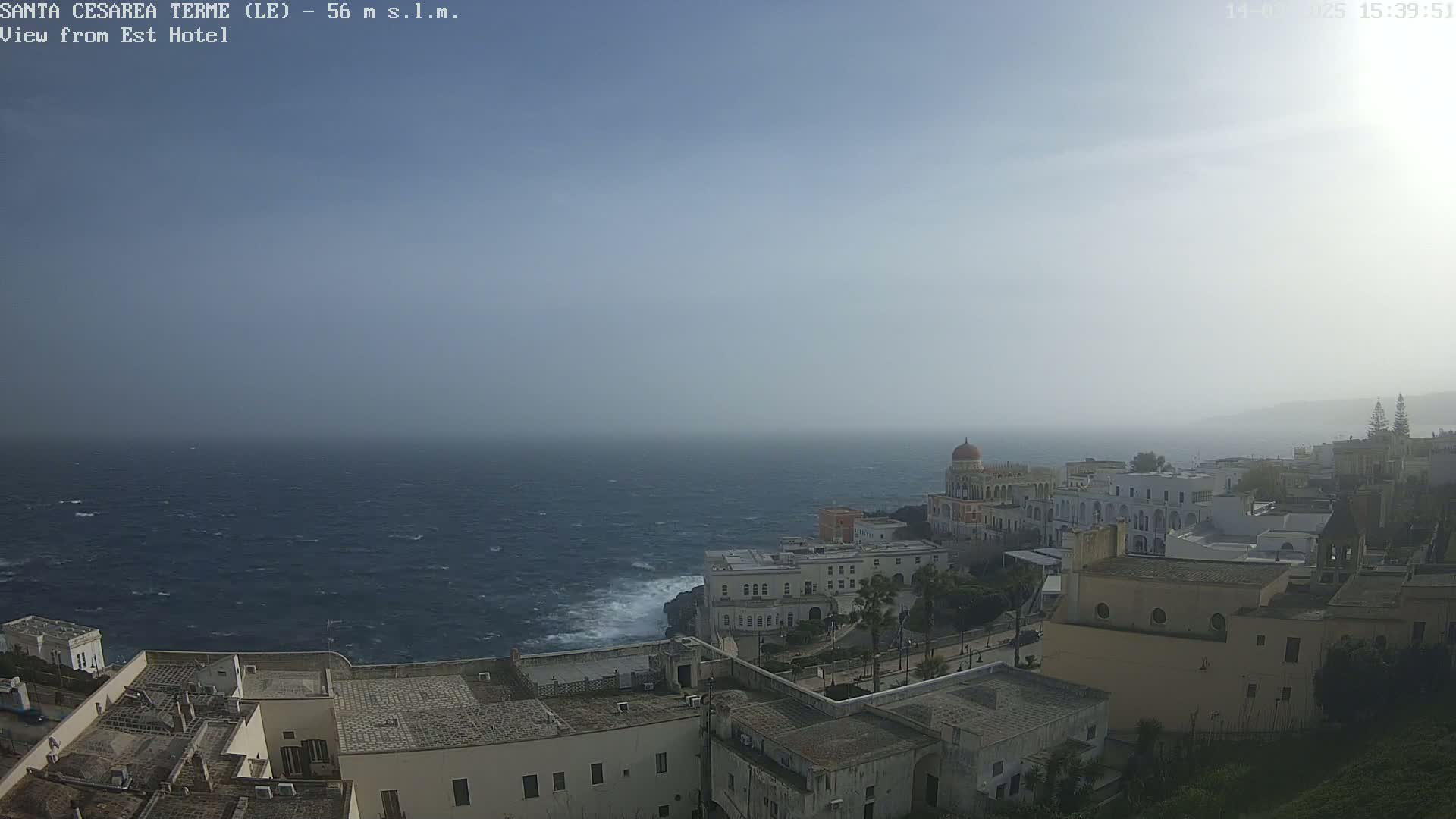 A hazy, windy day overlooks a coastal town with white buildings and a dark blue, choppy sea.