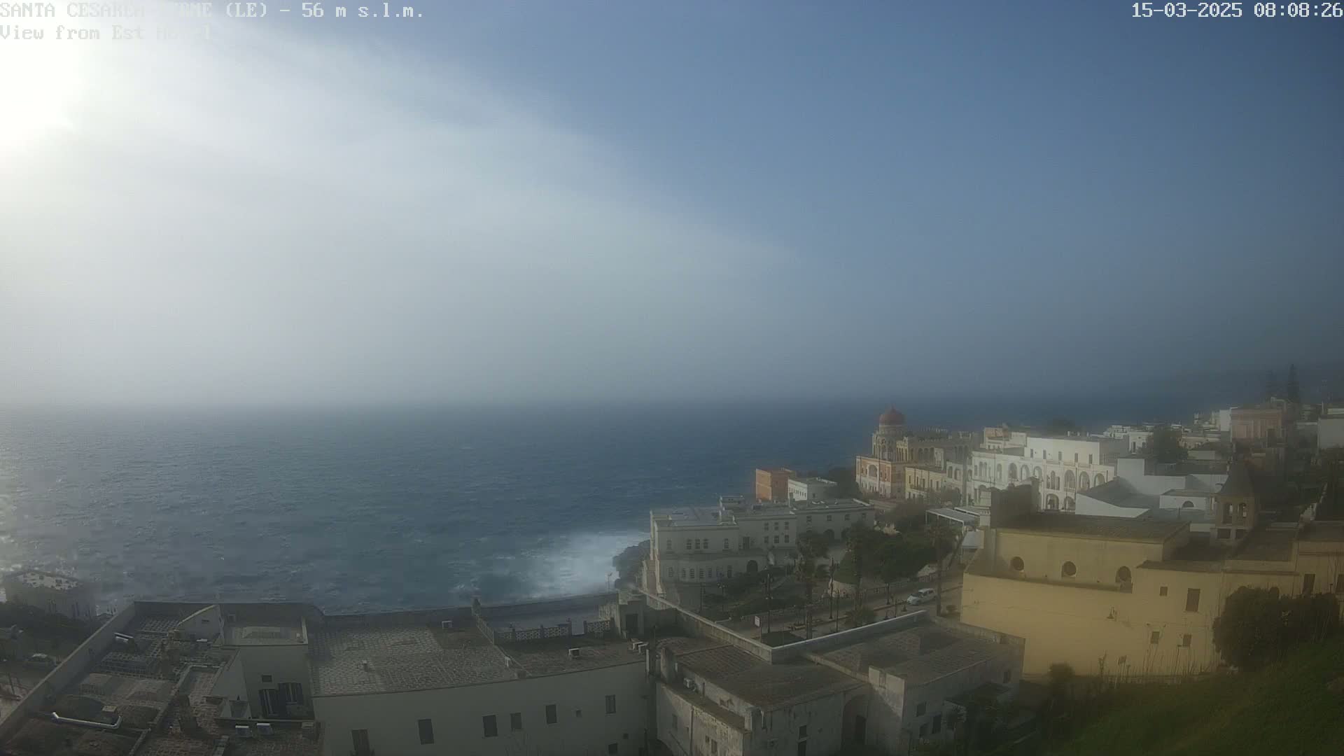 A hazy coastal town overlooks a dark blue, choppy sea under a mostly clear sky.