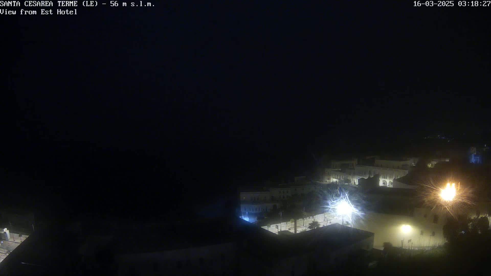 A nighttime, dark view of a town's illuminated buildings and streets, possibly under a cloudy or stormy sky.