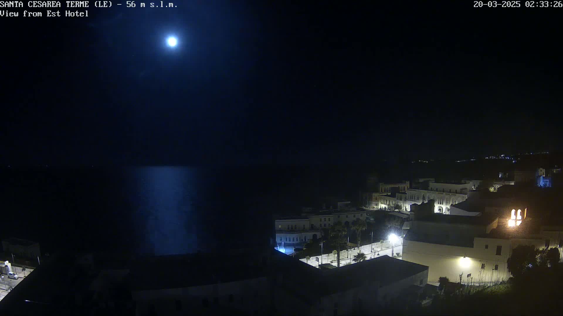 A bright moon illuminates a nighttime coastal town overlooking a dark sea.