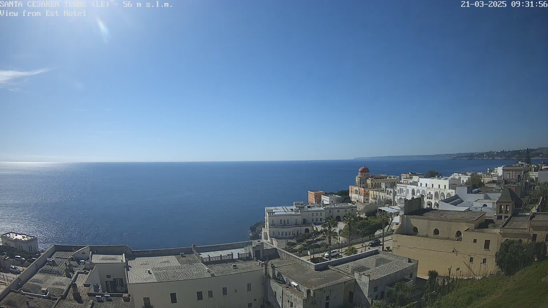 A coastal town with white buildings overlooks a calm blue sea under a clear blue sky.