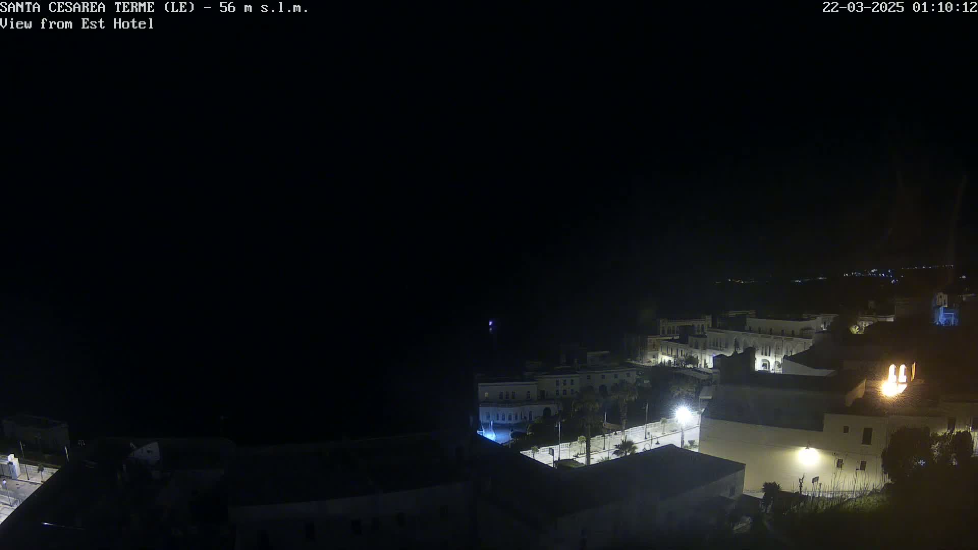 A nighttime, dark view of a coastal town with dimly lit buildings and a dark sea in the background.