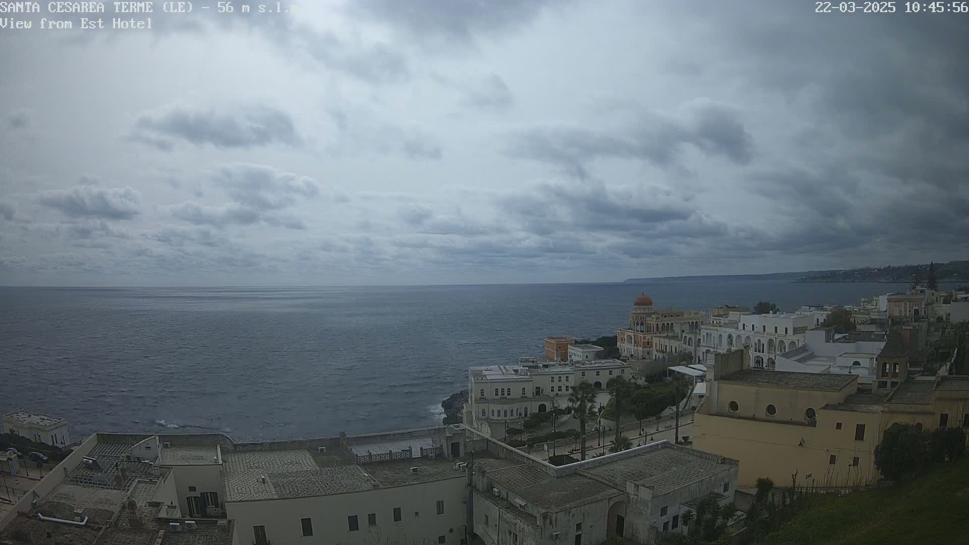 A coastal town with white buildings is nestled against a dark blue sea under a cloudy sky.