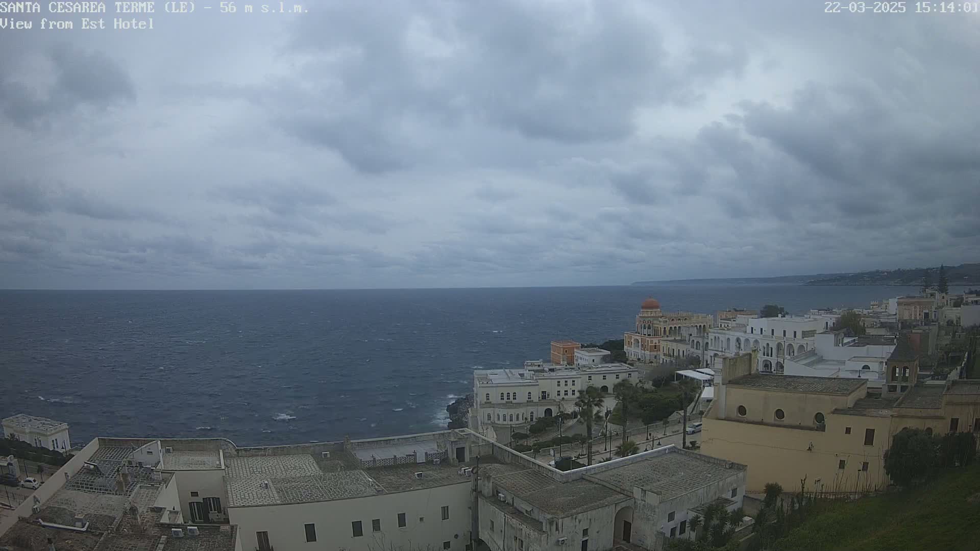 A coastal town with white buildings and a calm sea under a cloudy sky.