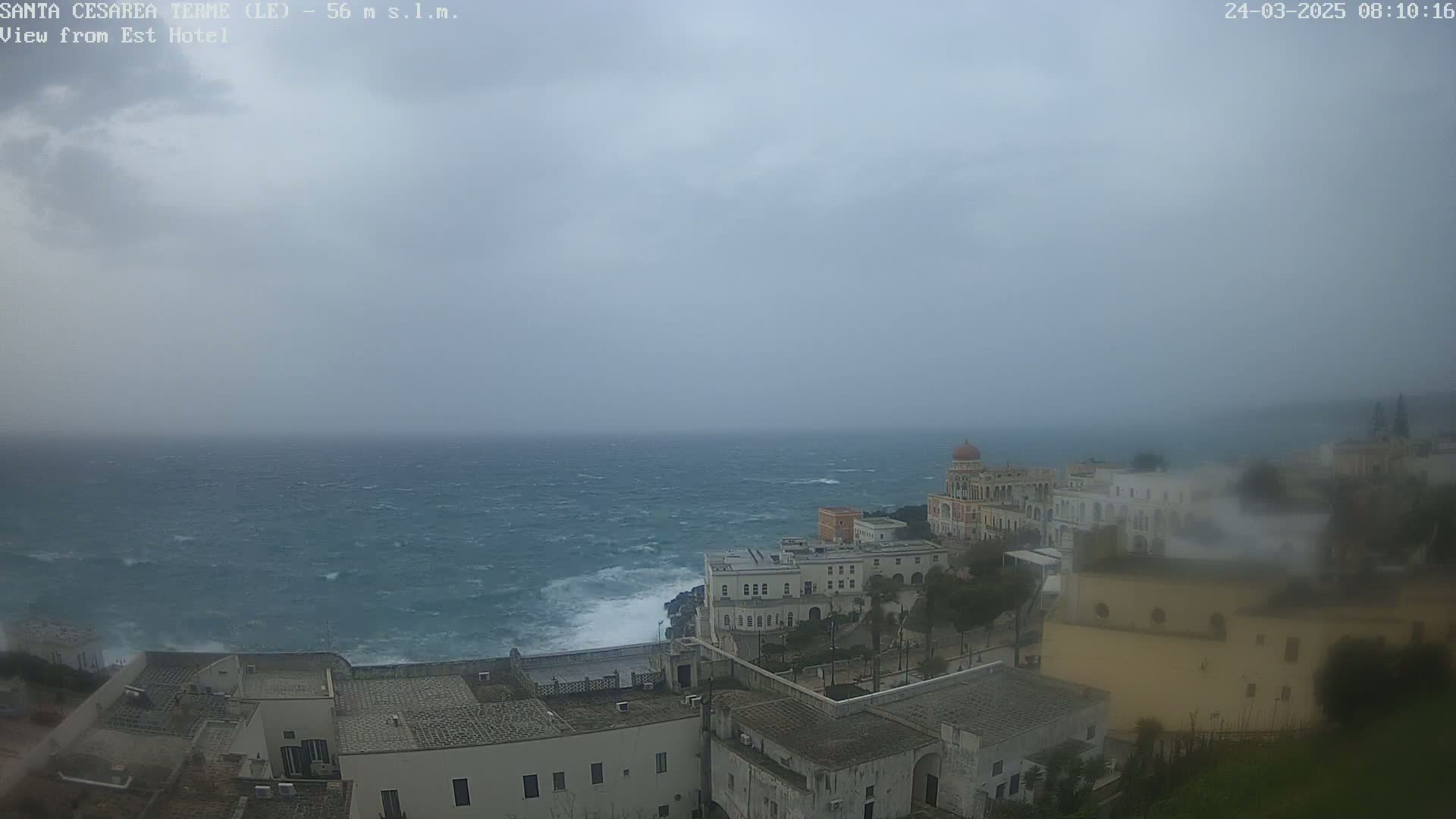 A coastal town with white buildings is shown on a blustery, overcast day, with a choppy sea extending to the horizon.