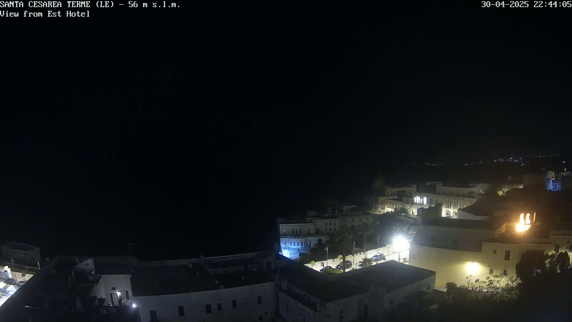 A nighttime, high-angle view shows a coastal town with buildings illuminated, under a dark, clear sky.