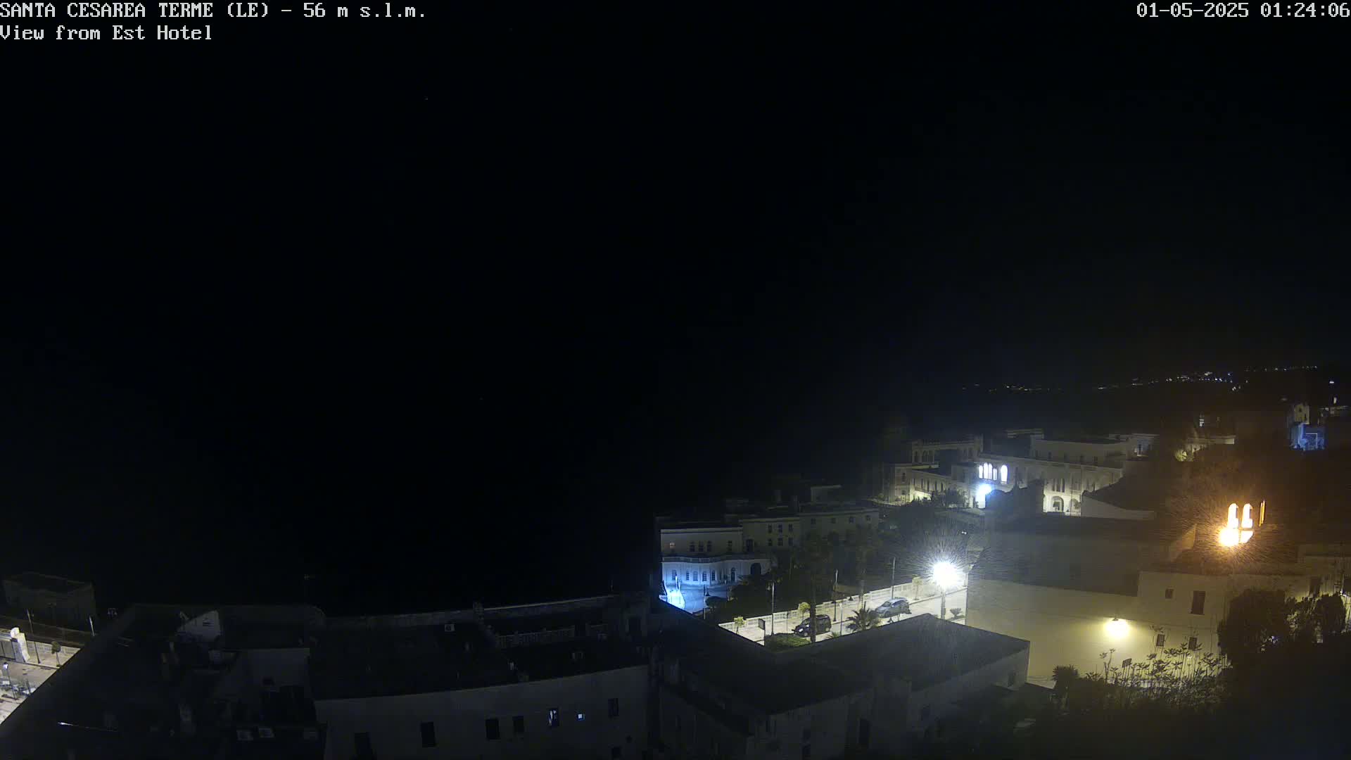 A nighttime, overhead view of a coastal town with dimly lit buildings and streets, under a clear, dark sky.