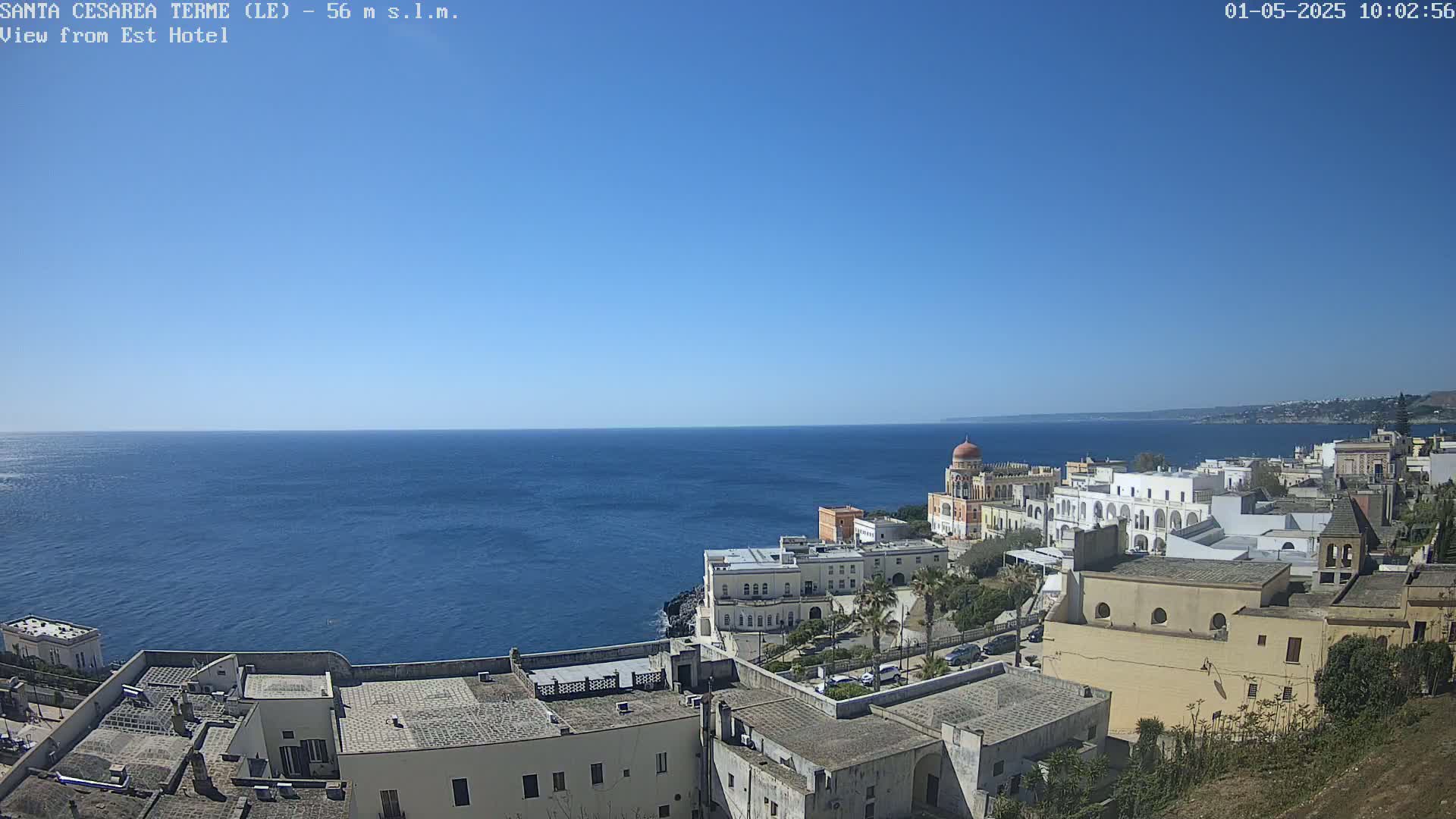 A clear, sunny day overlooks a coastal town with white buildings and a calm blue sea.