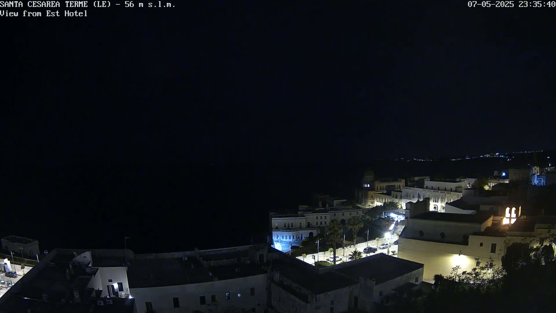 A nighttime, high-angle view of a coastal town with buildings illuminated, overlooking a dark body of water under a clear, dark sky.