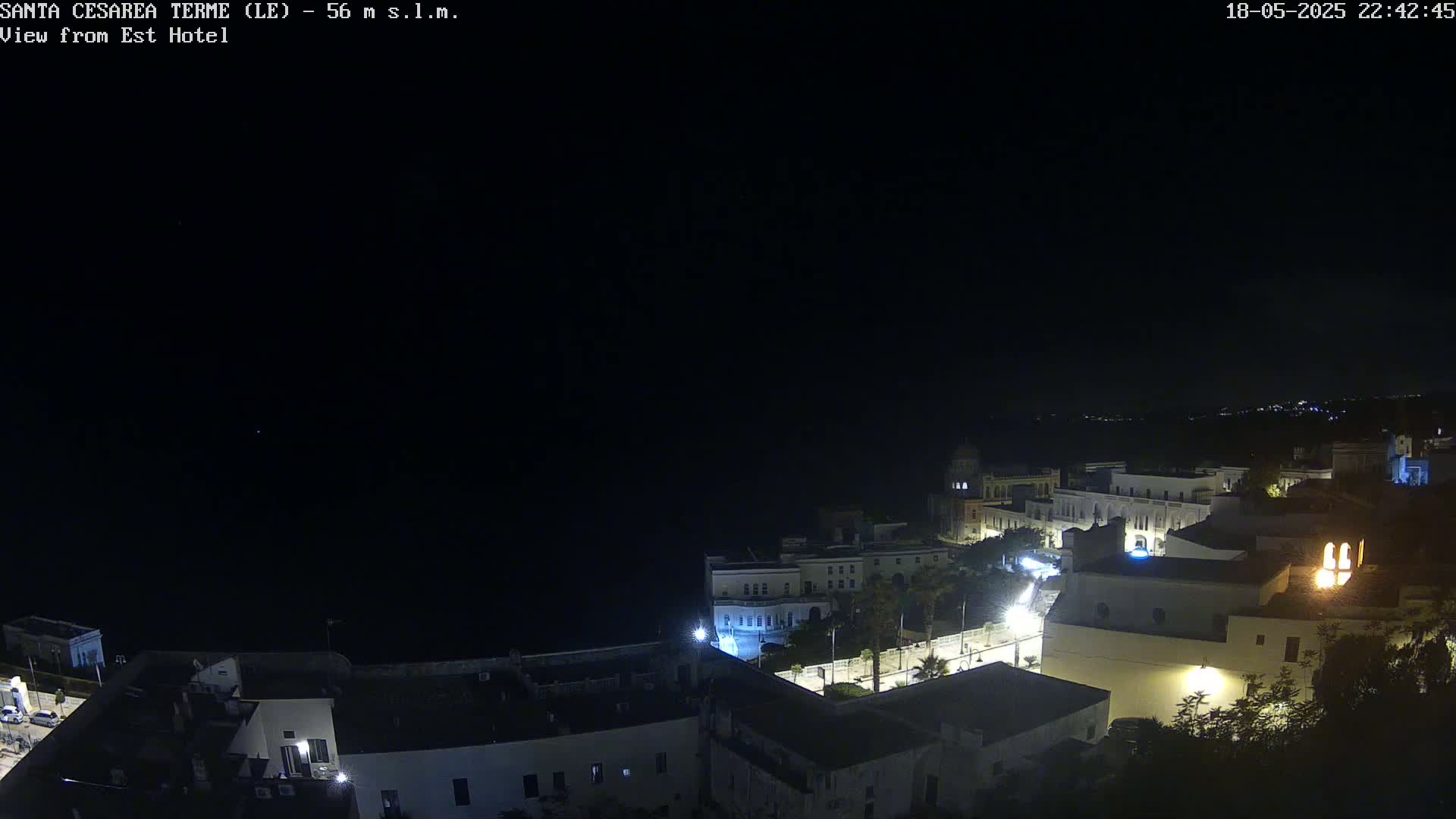A nighttime, high-angle view of a coastal town with buildings illuminated against a dark sky.