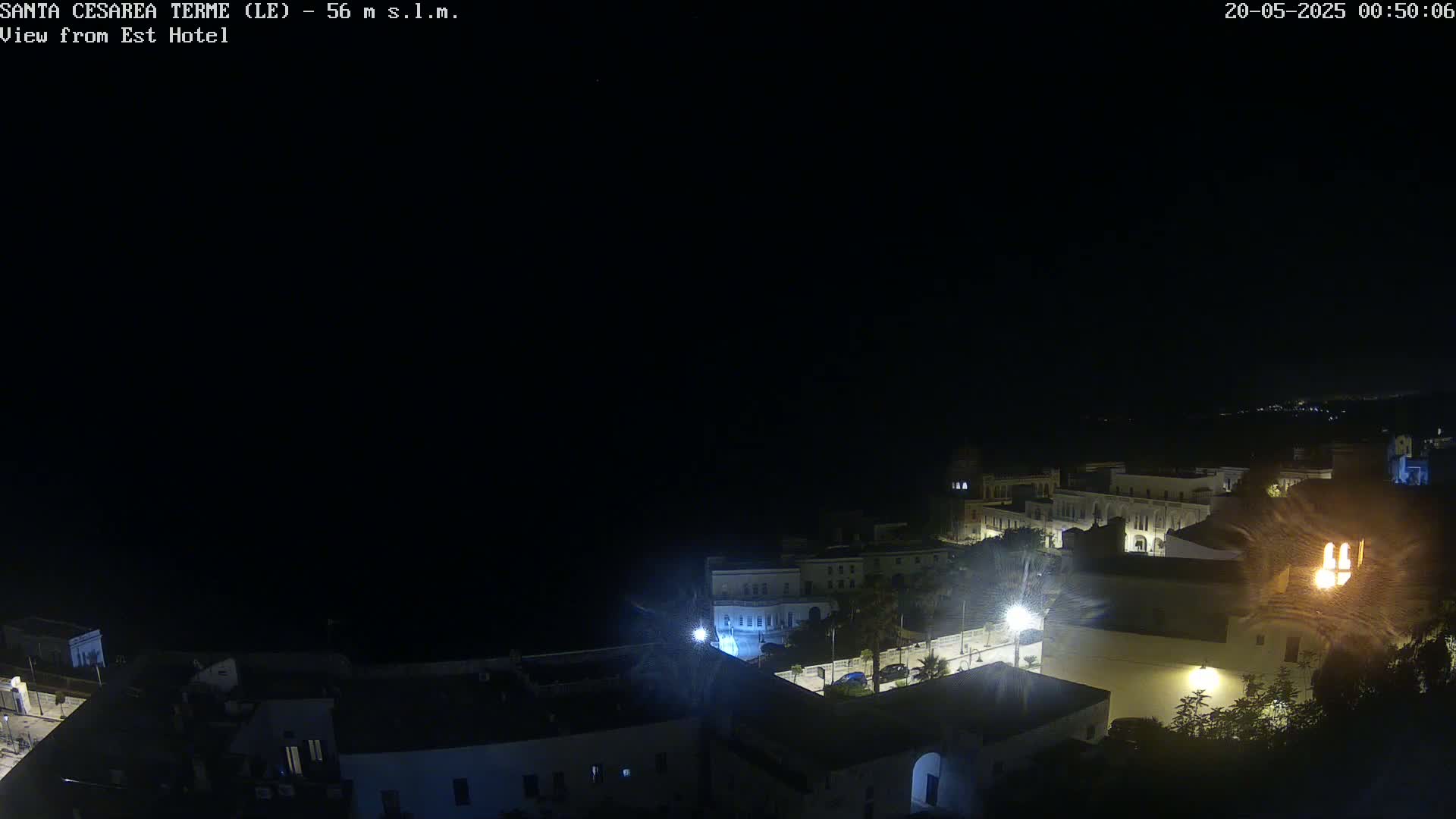 A nighttime, aerial view of a coastal town with buildings illuminated, under a clear, dark sky.