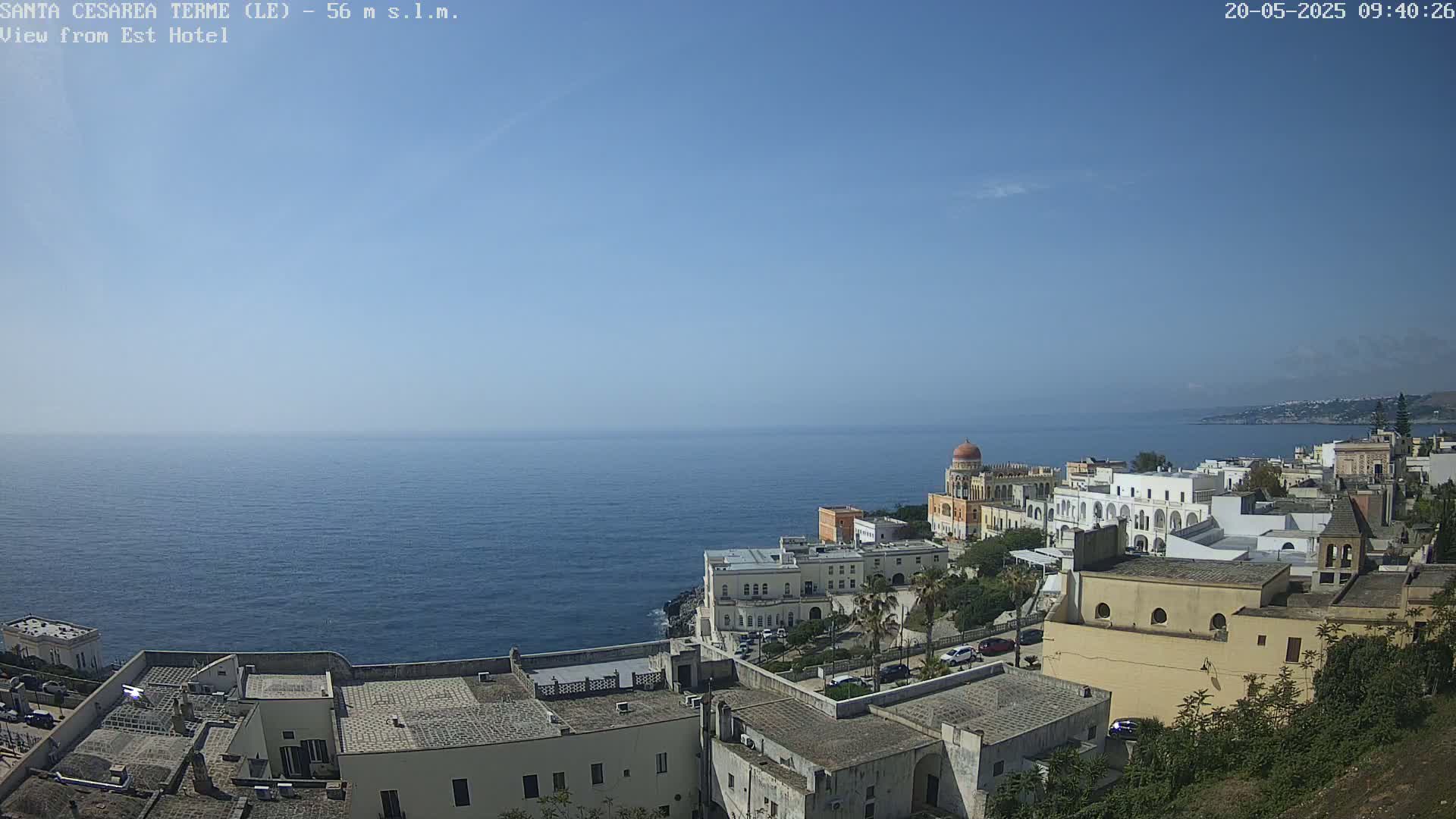A coastal town overlooks a calm, blue sea under a clear, sunny sky.