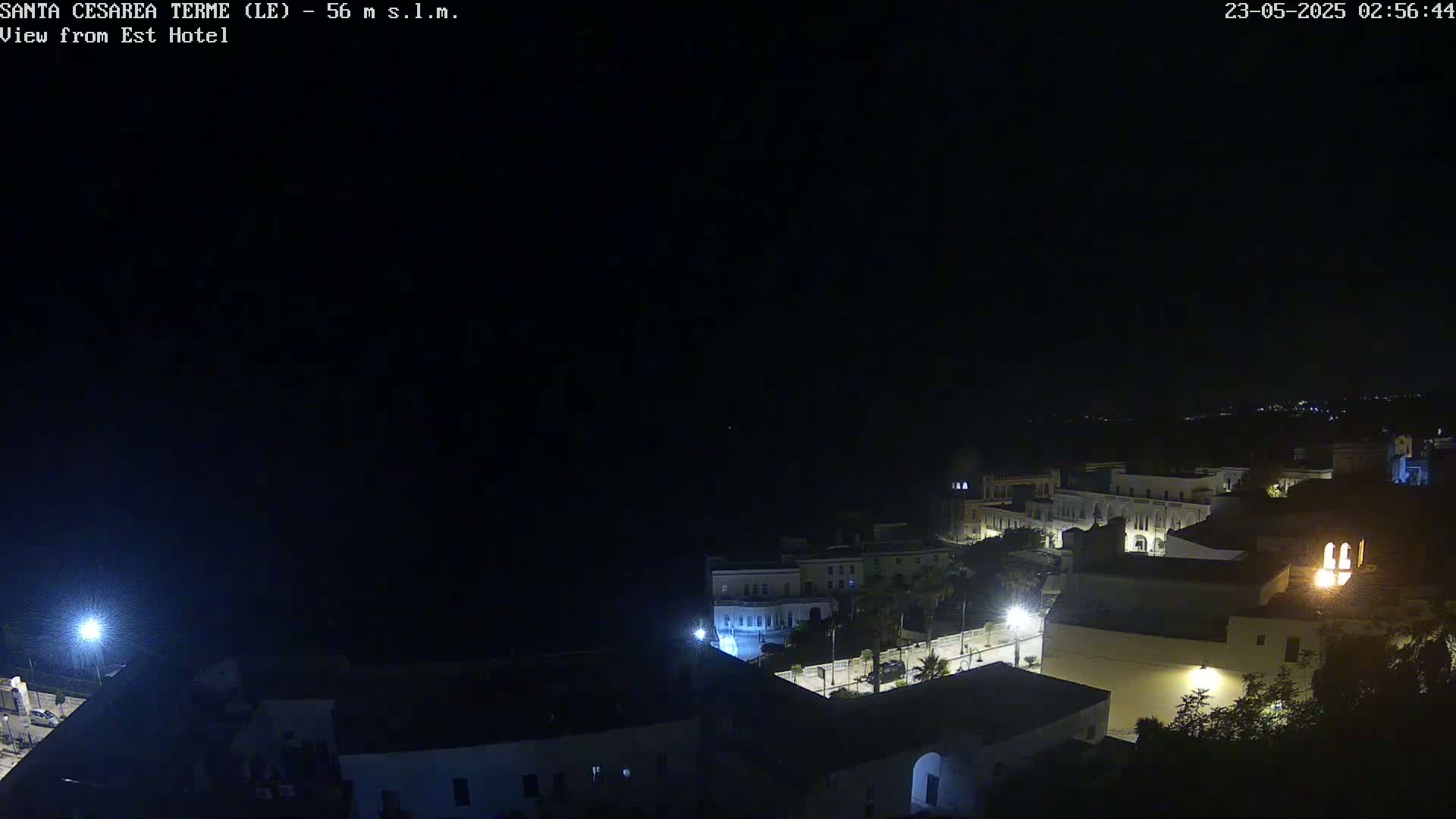 A nighttime, high-angle view of a coastal town with dimly lit buildings and a dark sea.