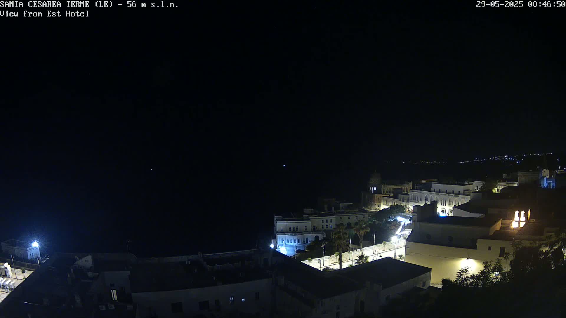 A nighttime, high-angle view shows a coastal town with buildings illuminated against a dark sky.