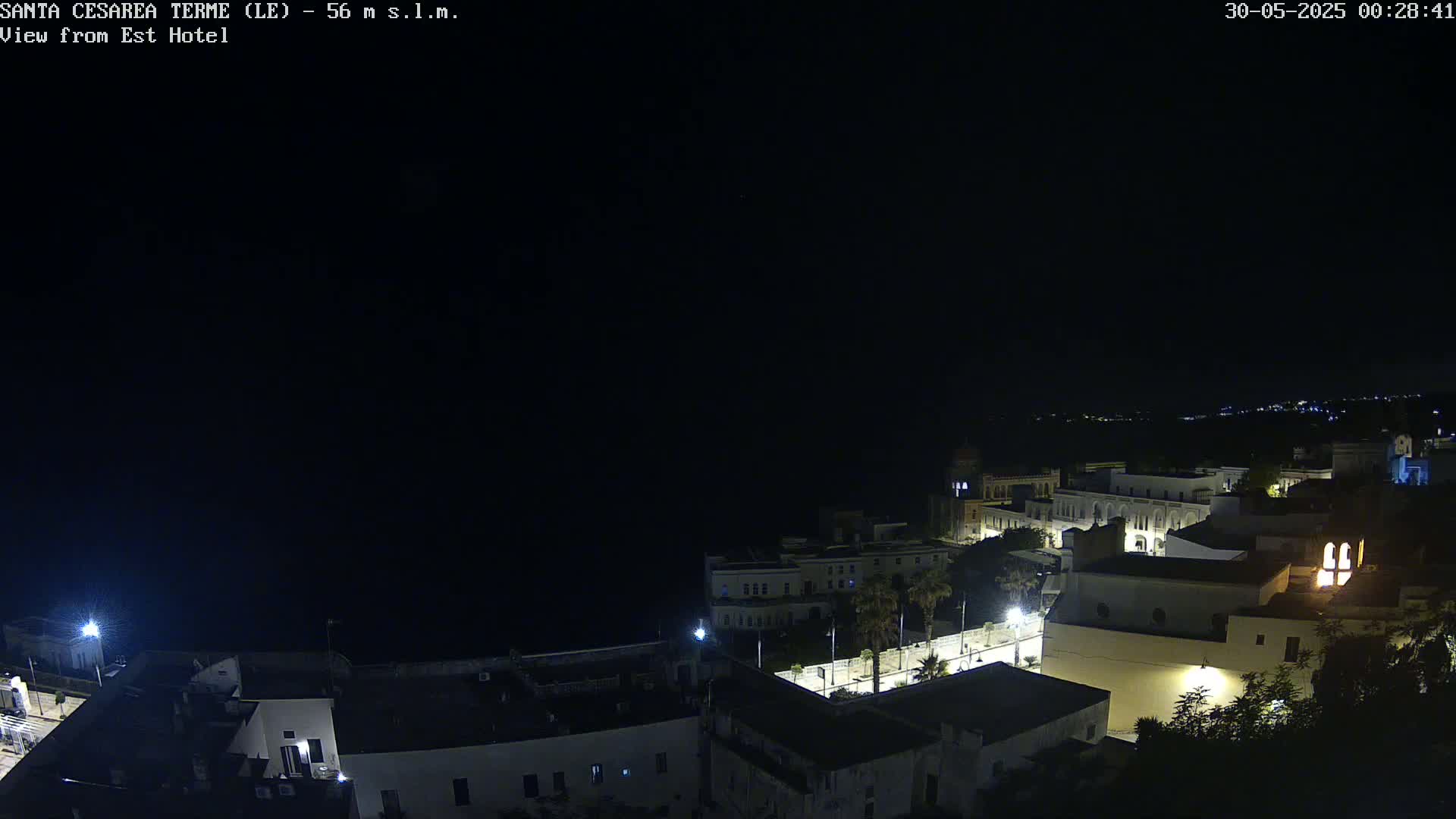 A nighttime, high-angle view of a coastal town, with buildings illuminated against a dark sea and sky.