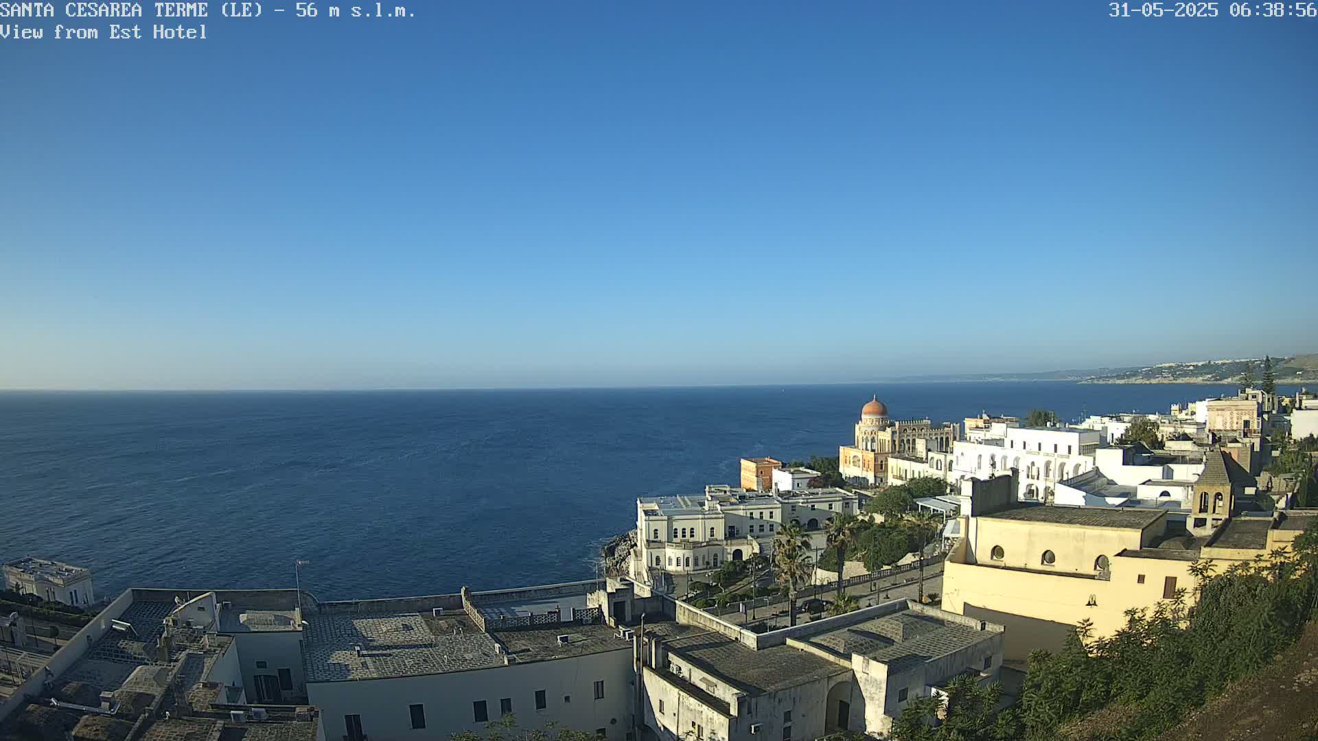 A coastal town with white buildings overlooks a calm blue sea under a clear blue sky.