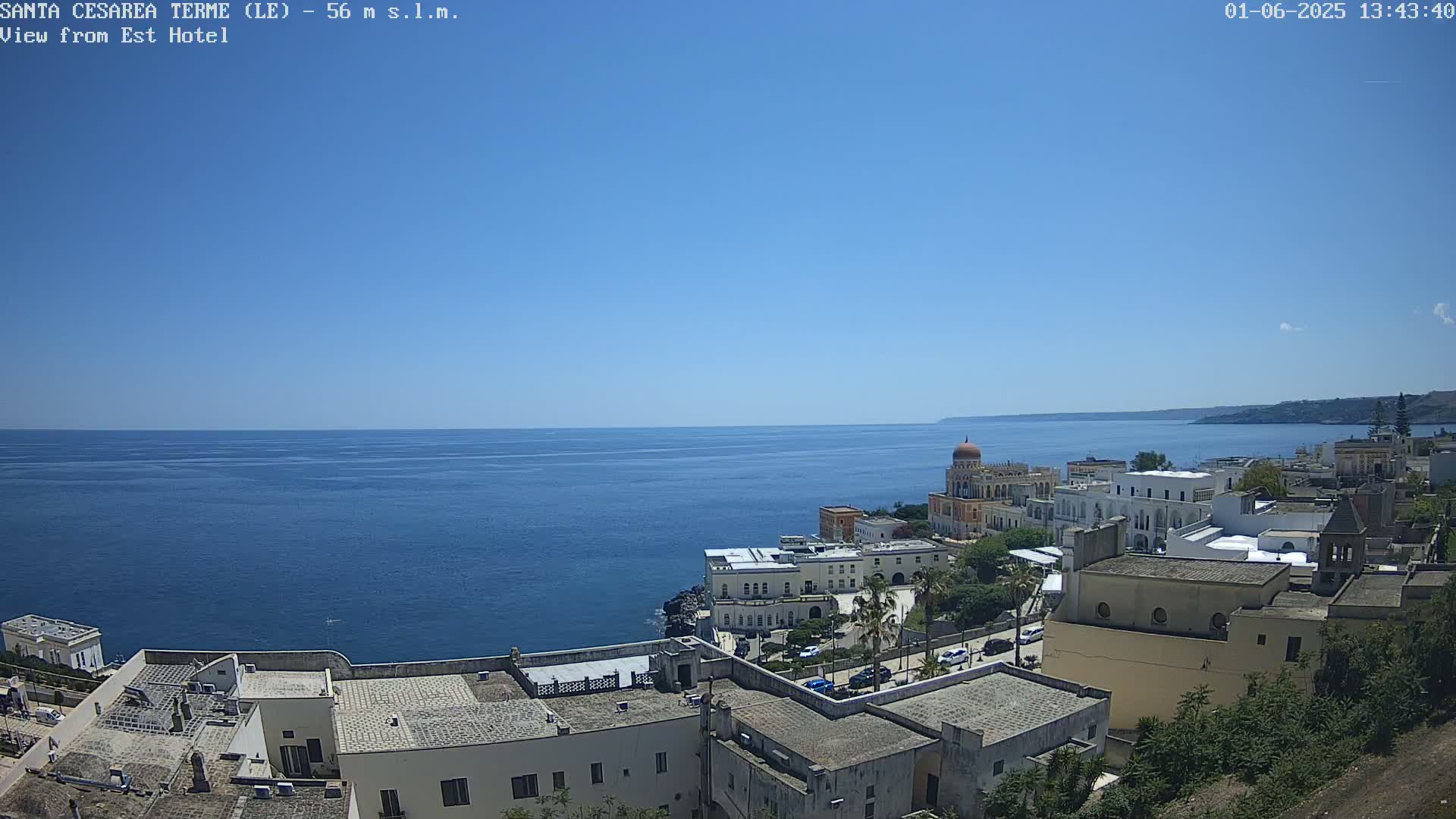 A coastal town with white buildings and a calm blue sea under a clear blue sky.