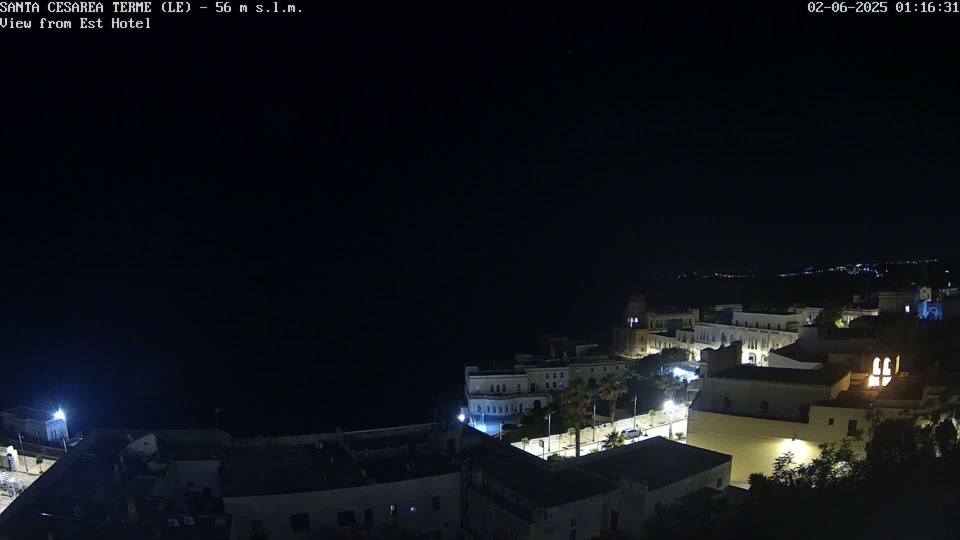 A nighttime aerial view of a coastal town with buildings illuminated, under a clear, dark sky.