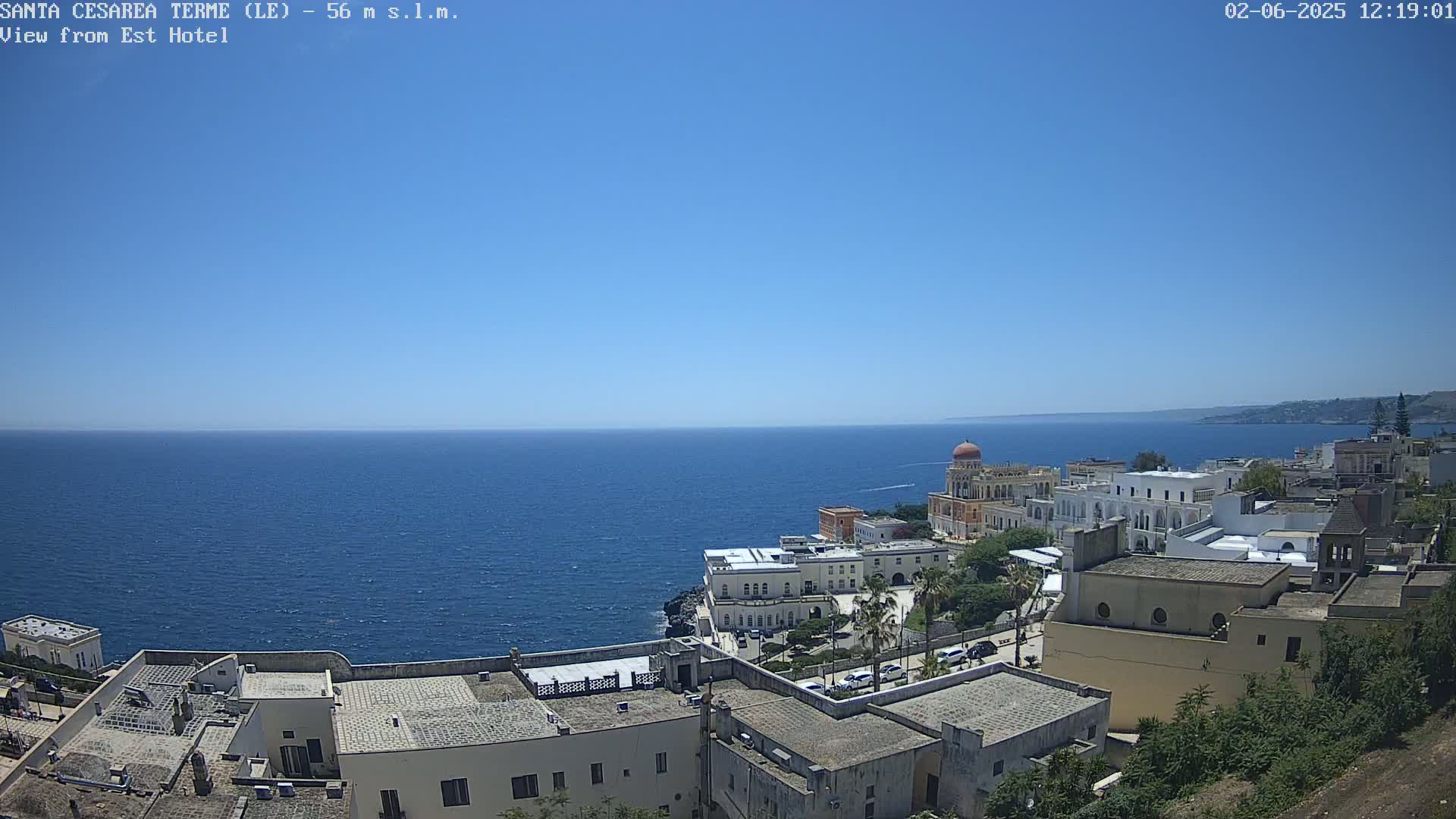 A clear, sunny day overlooking a coastal town with white buildings and a calm blue sea.