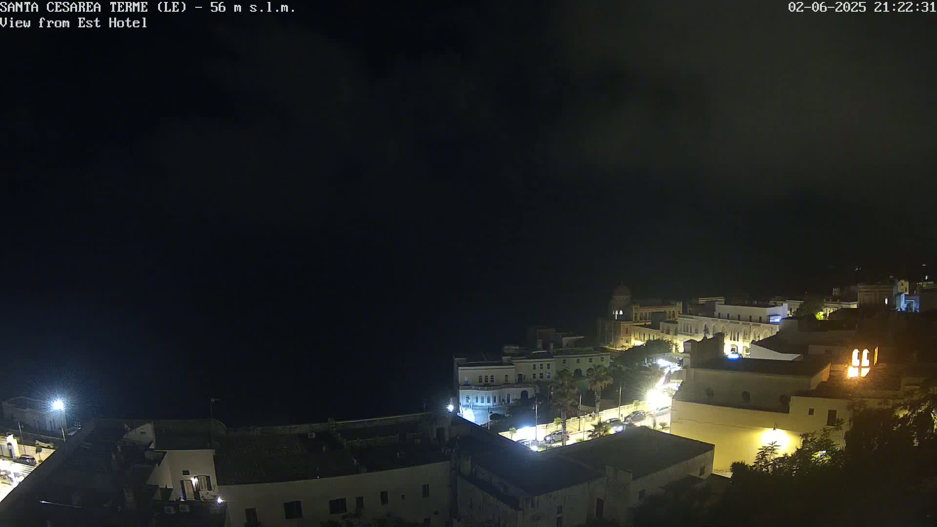 A nighttime view of a coastal town with dimly lit buildings and streets under a dark, cloudy sky.