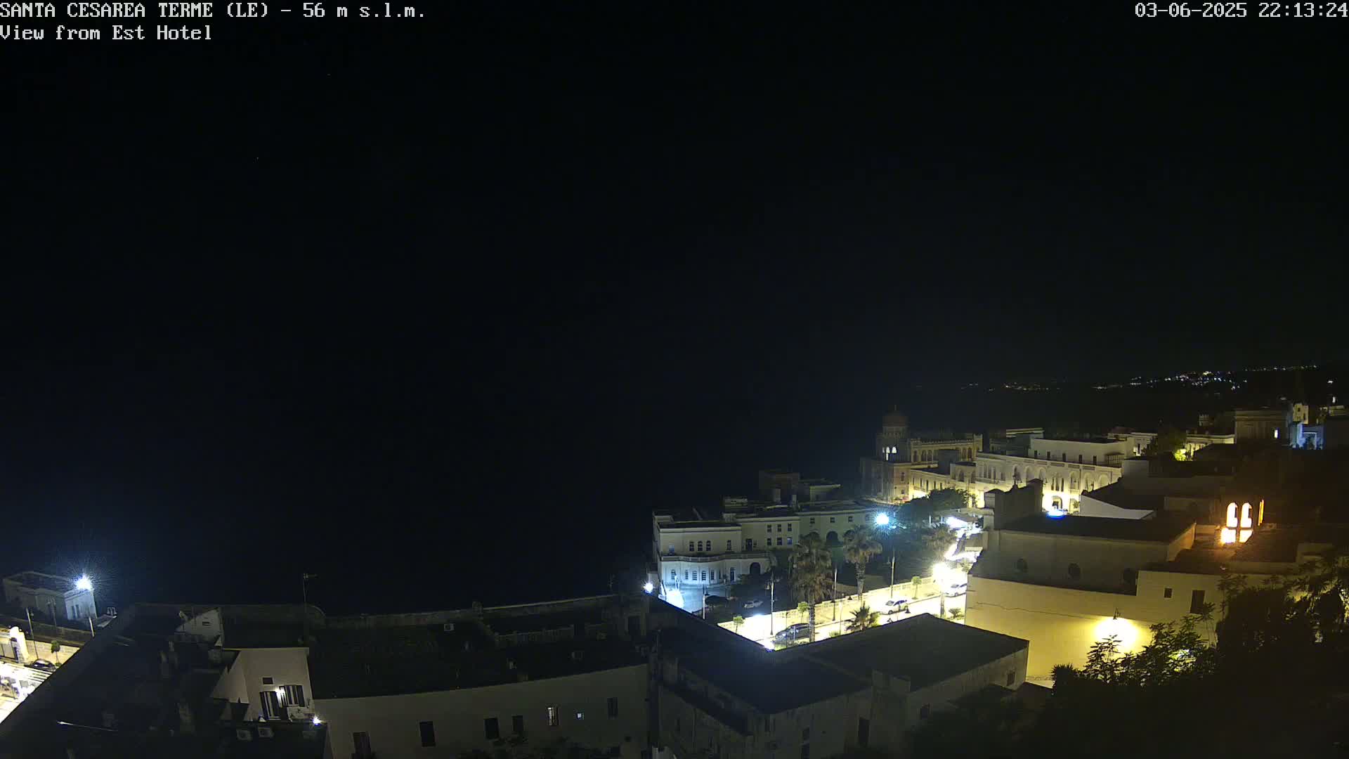 A nighttime, high-angle view of a coastal town with buildings illuminated, under a clear, dark sky.