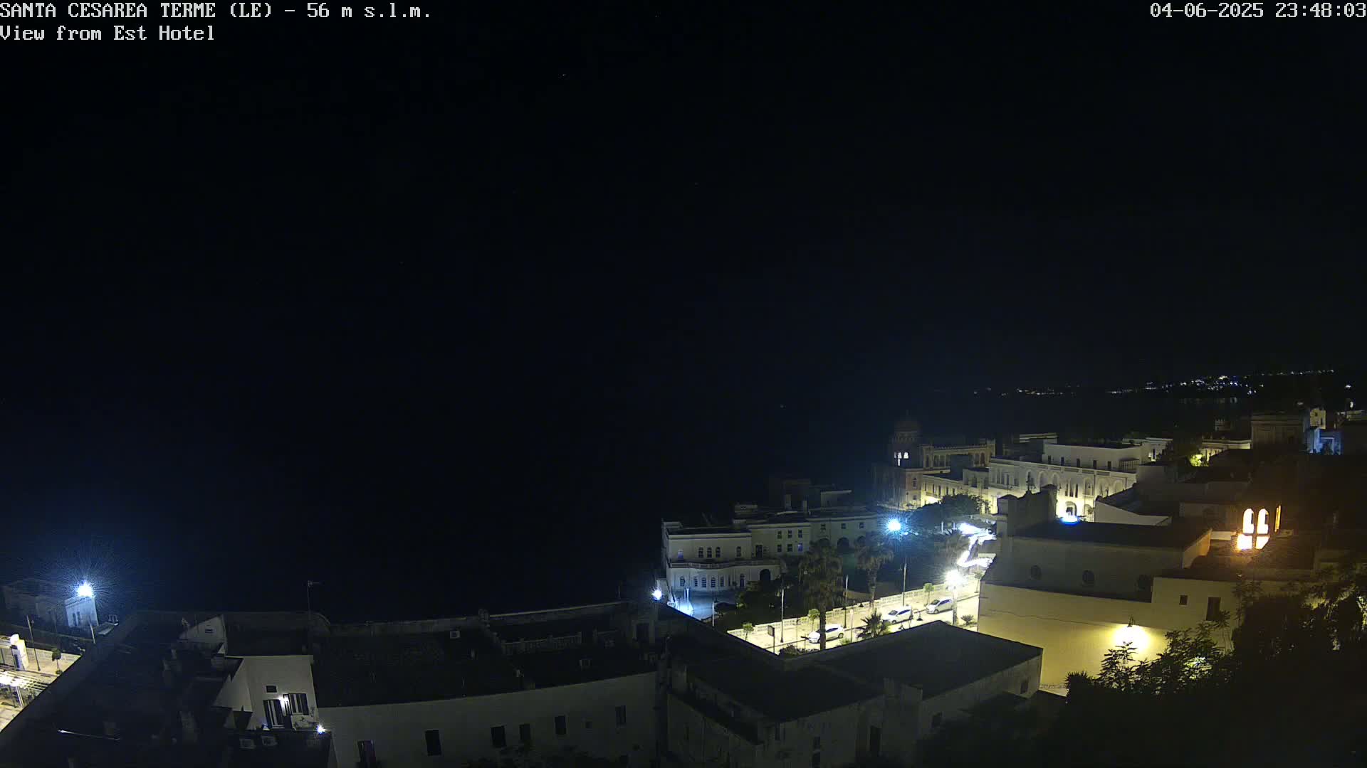 A nighttime, high-angle view of a coastal town with buildings illuminated against a dark sky.