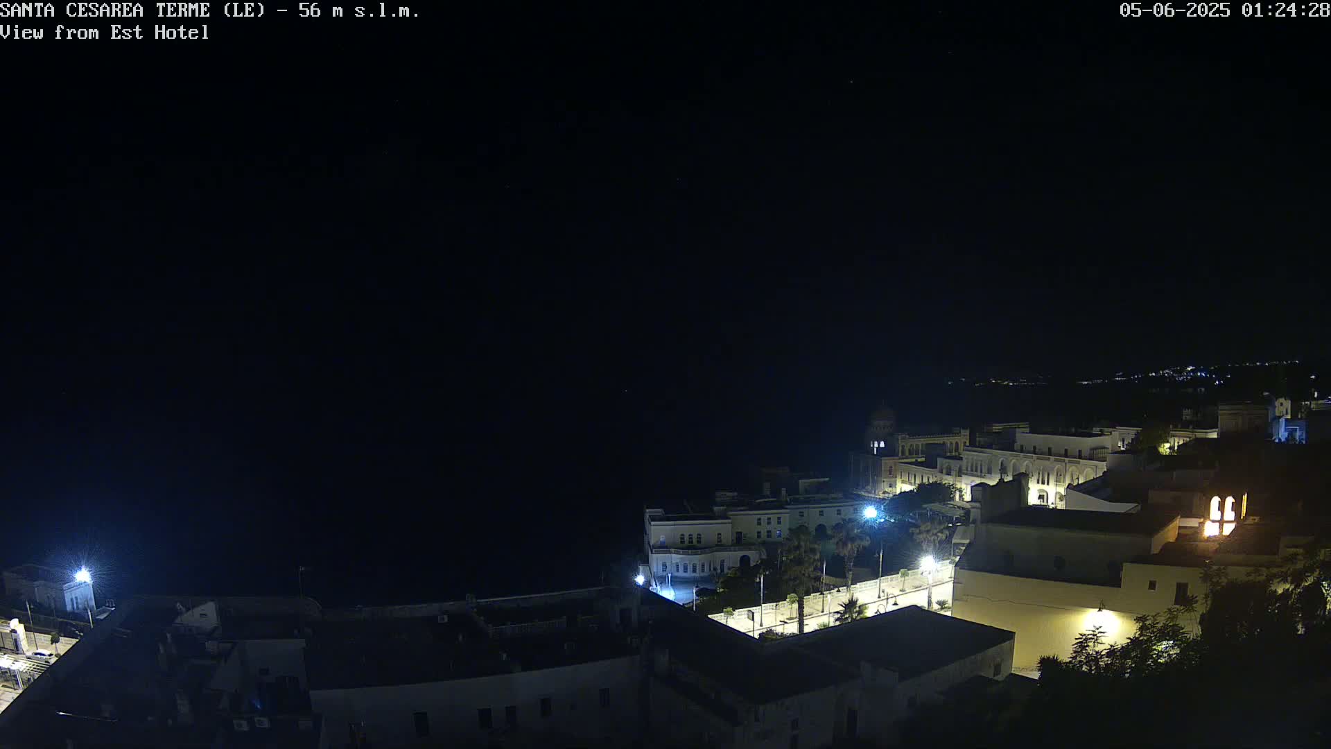 A nighttime, aerial view of a coastal town with buildings illuminated, under a clear, dark sky.