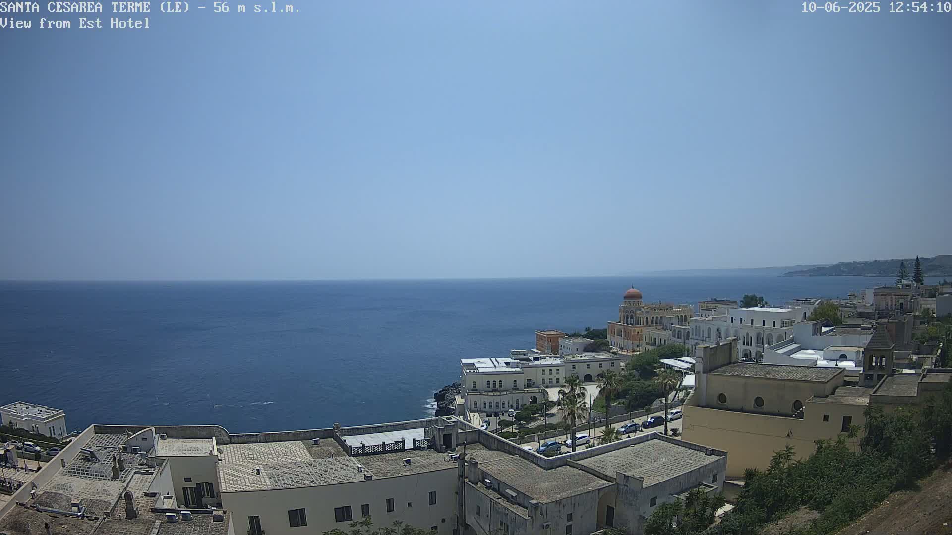 A clear, sunny day overlooks a coastal town with white buildings and a calm blue sea.