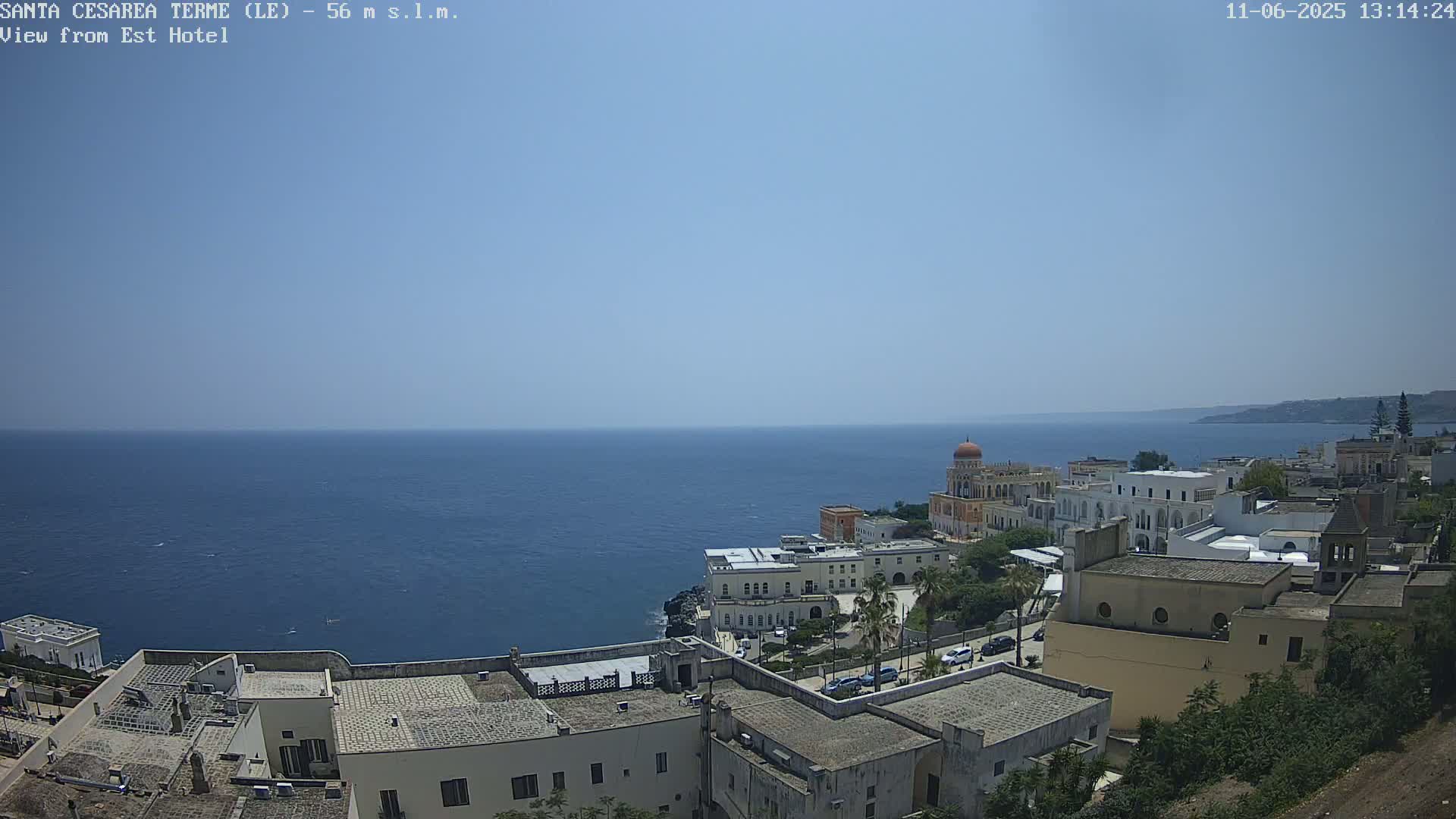A coastal town with white buildings overlooks a calm blue sea under a clear sky.