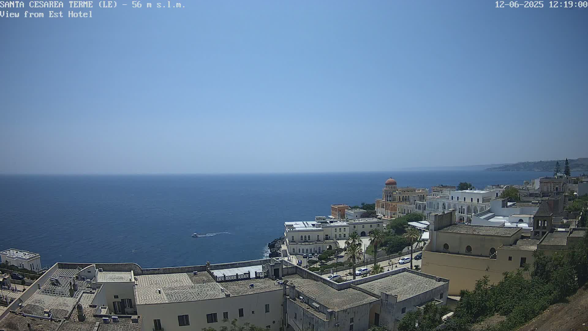 A coastal town with white buildings and a calm blue sea under a clear blue sky is visible from an elevated vantage point.