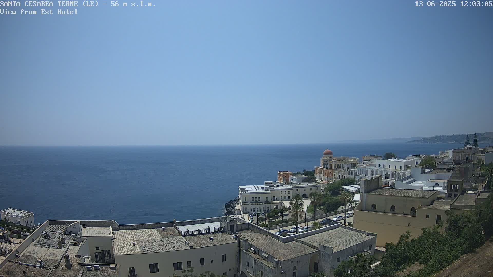 A coastal town with white buildings overlooks a calm blue sea under a clear, sunny sky.