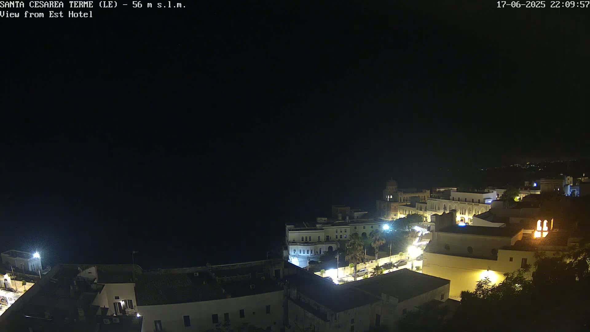 A nighttime, aerial view of a coastal town with illuminated buildings and a dark sea under a clear sky.