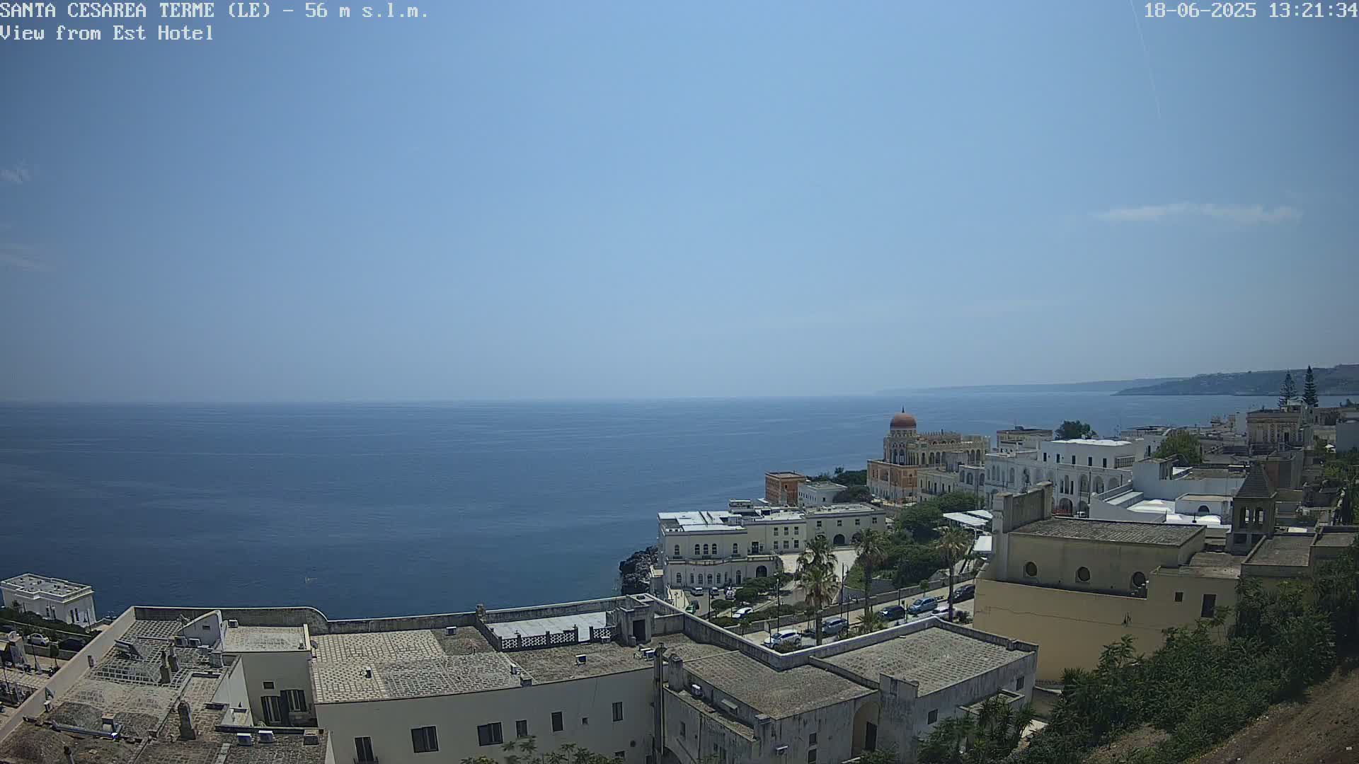 A coastal town with white buildings overlooks a calm, blue sea under a clear sky.