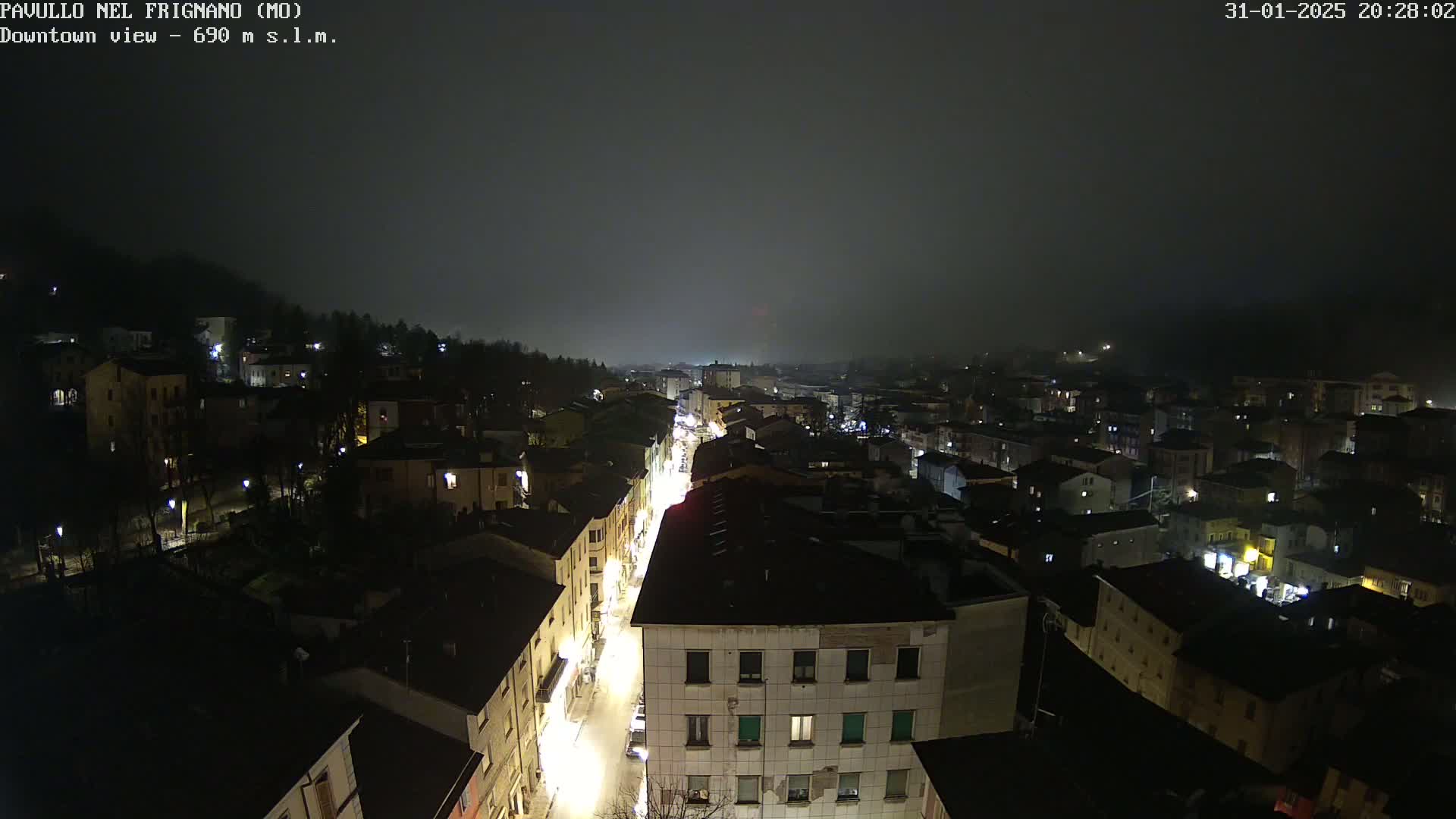 A nighttime, foggy view of a town's downtown area, showing illuminated streets and buildings.